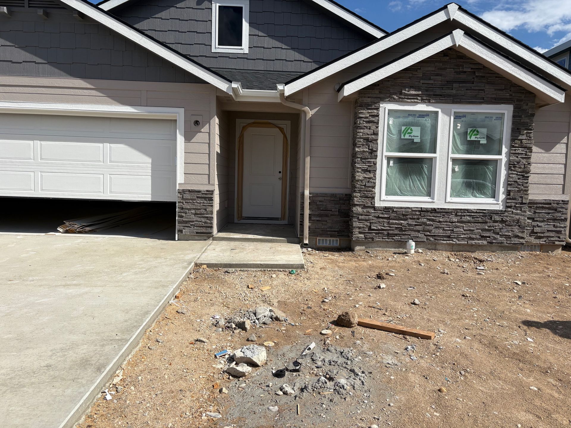 New house exterior with garage, front door, and stone accents. Construction site in front.
