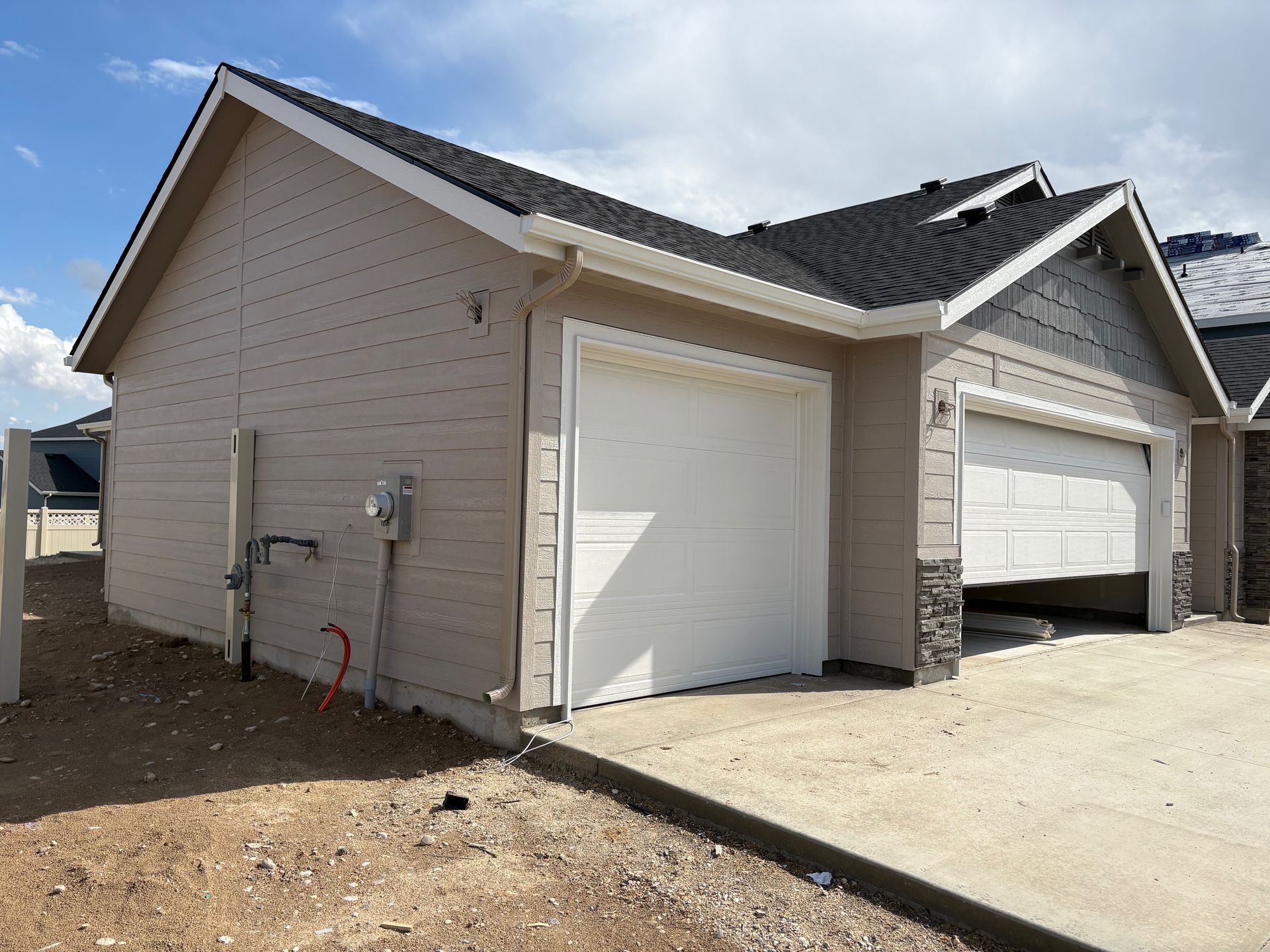 Beige and brown two-car garage with one door open, concrete driveway, and overcast sky.