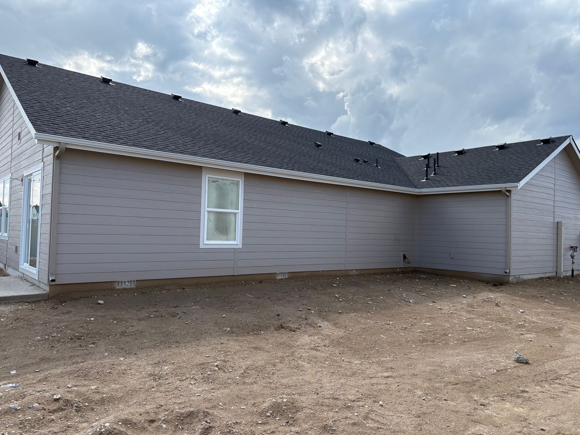 New house exterior with gray siding, dark roof, and cloudy sky. Unfinished yard.