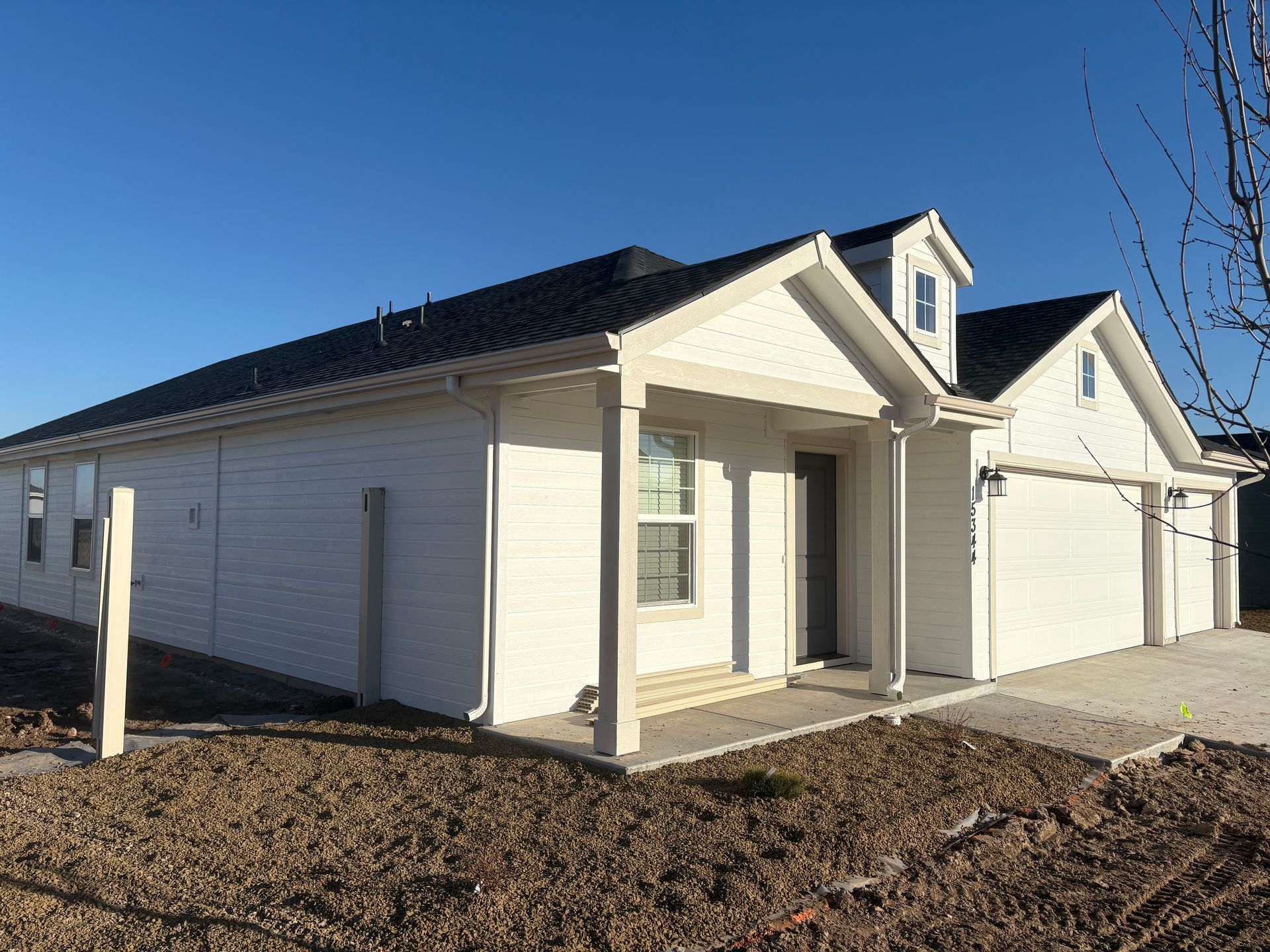 White house with black roof, small porch, and attached garage on a clear day.