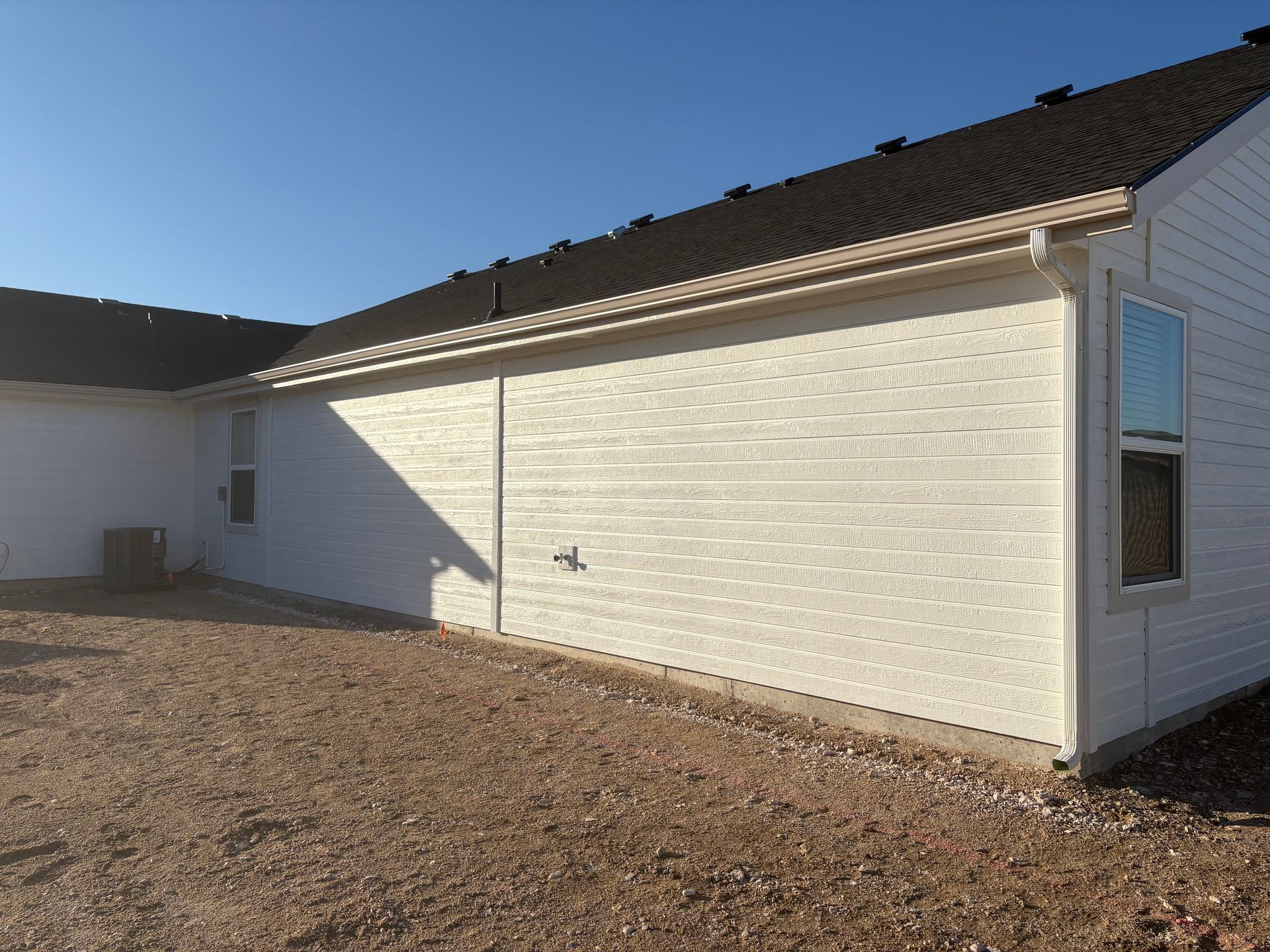 Exterior view of a white brick building with a dark roof and gravel ground under a clear blue sky.