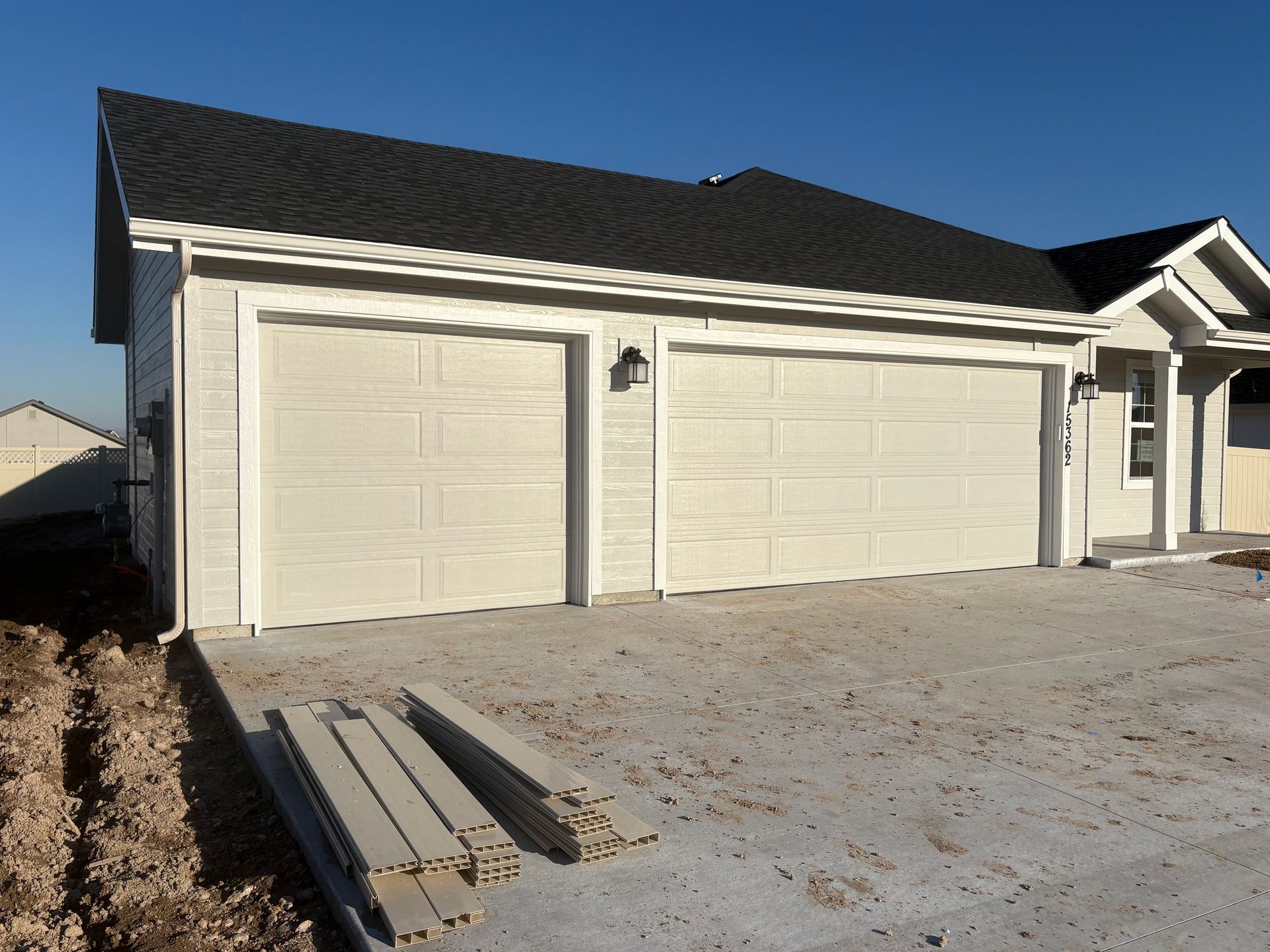 Two-car garage with light-colored doors and trim, black roof, and concrete driveway.
