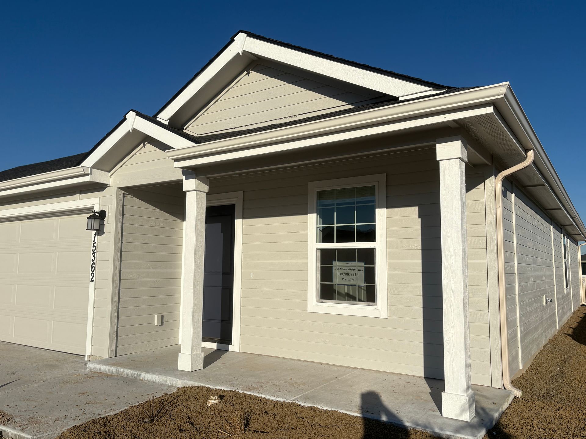 Beige house with white trim, a small porch, and a blue sky.