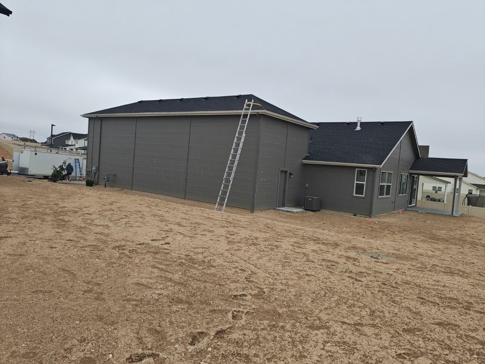 Gray house with a ladder leaning against it on a gravelly hill, cloudy sky.
