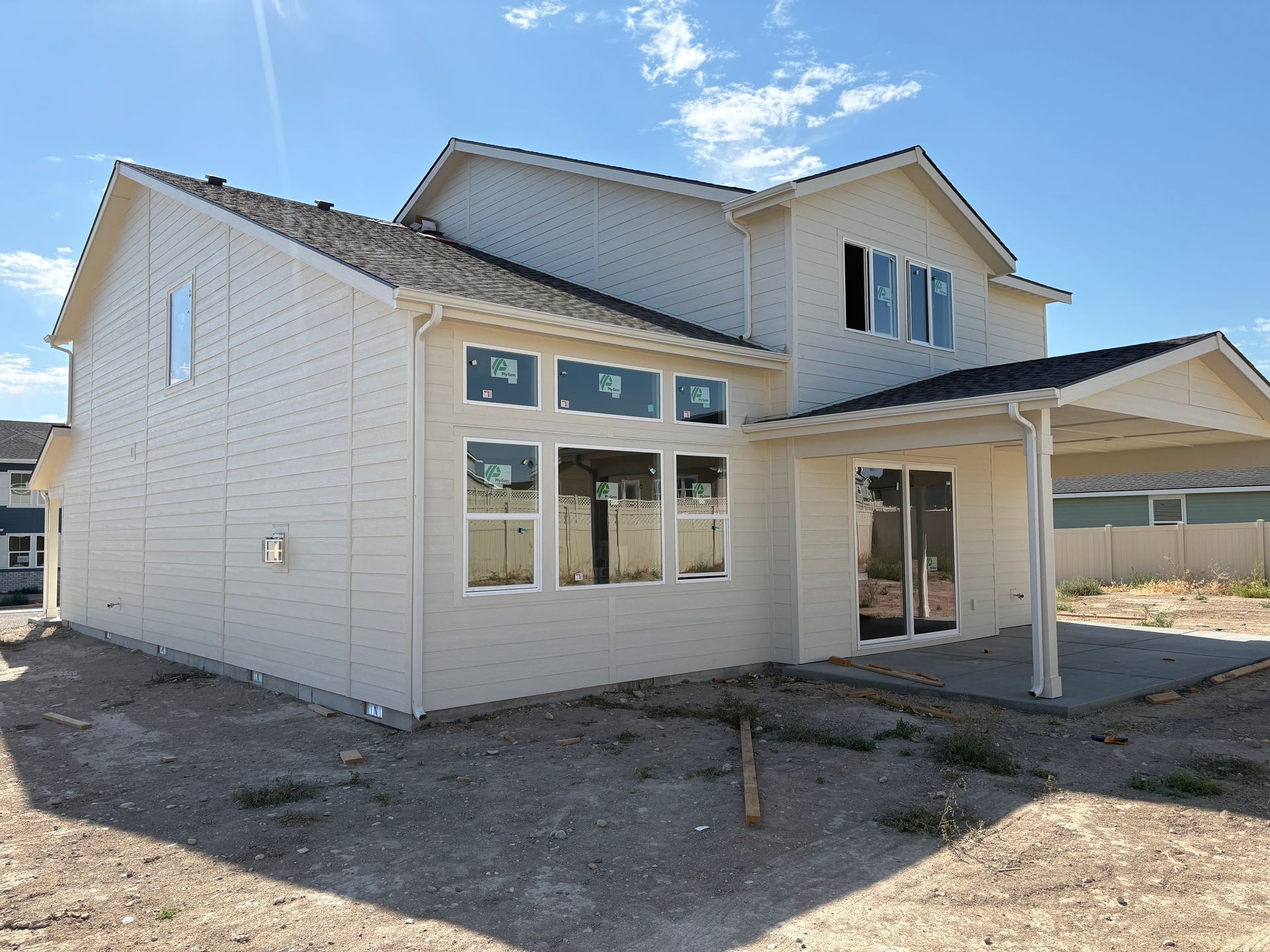 Back of a two-story beige house under construction with large windows and a covered patio, set against a blue sky.