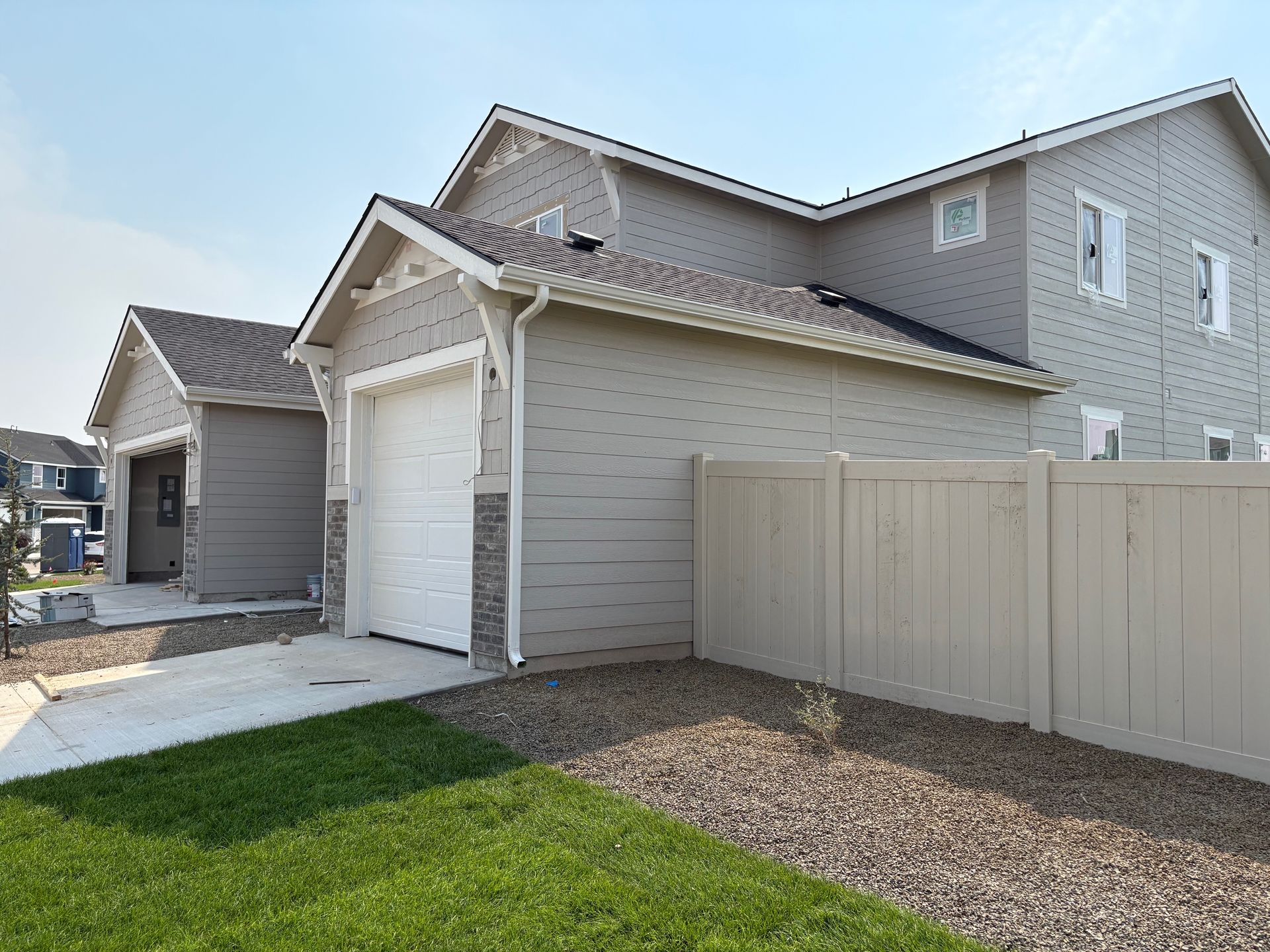A two-story house with a detached garage and a tan fence. It has a white garage door and gray siding.