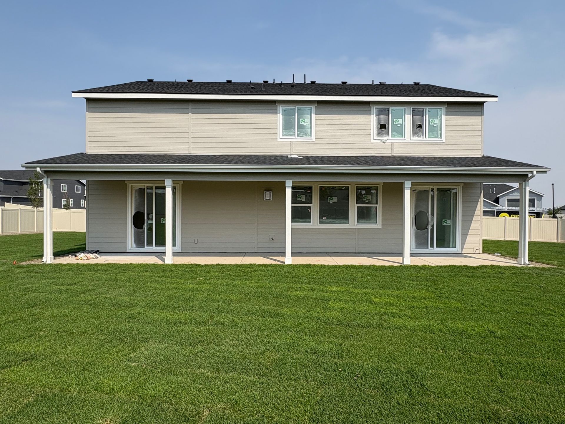 Two-story beige house with a covered patio and green lawn against a blue sky.
