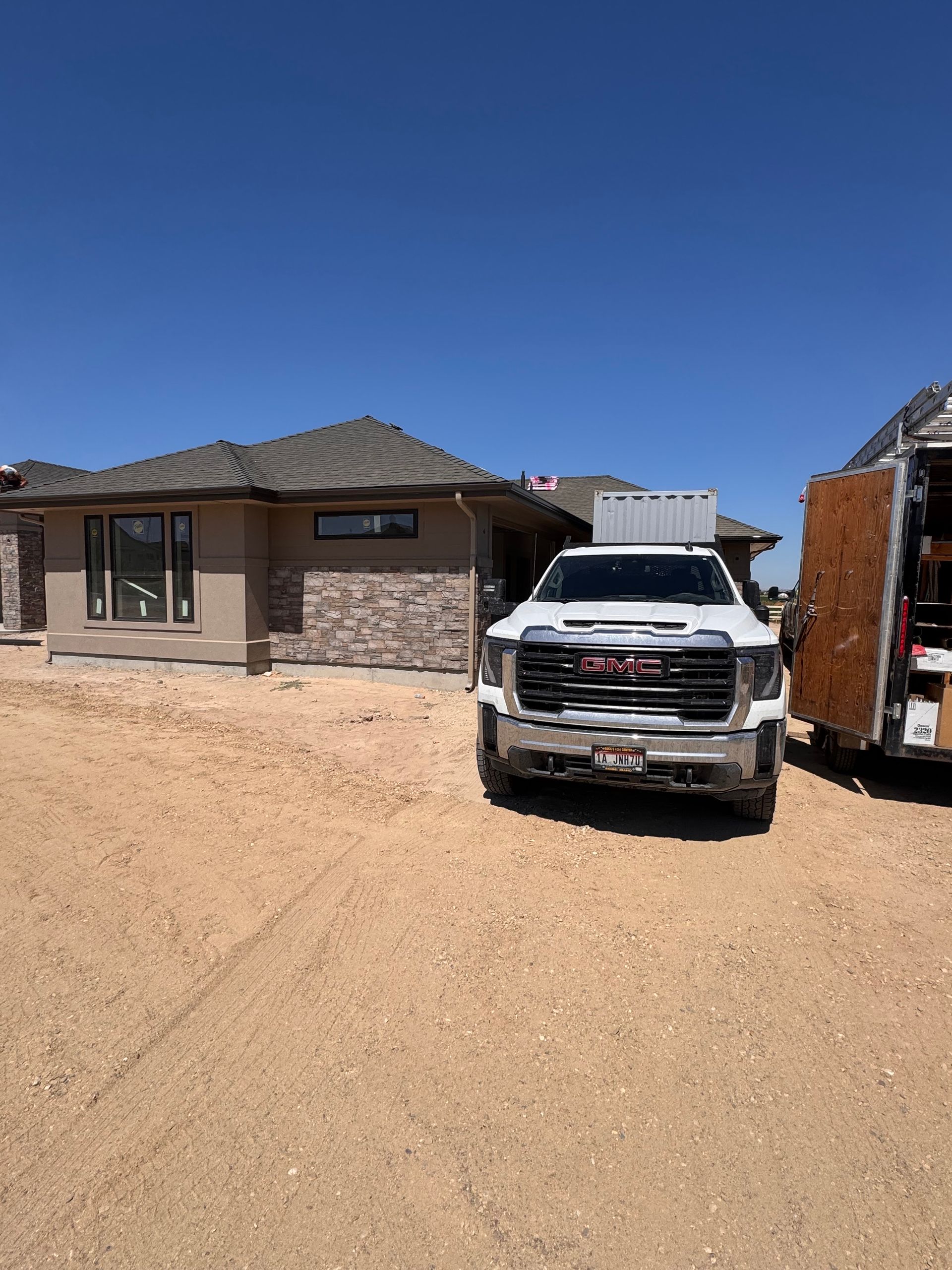 White GMC truck parked in front of a partially constructed house on a sunny day.
