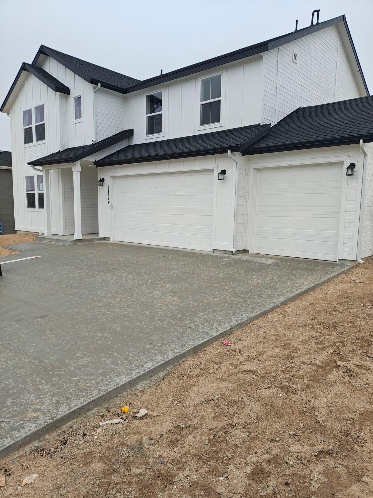 White house with black roof, three-car garage, and newly poured concrete driveway on a cloudy day.