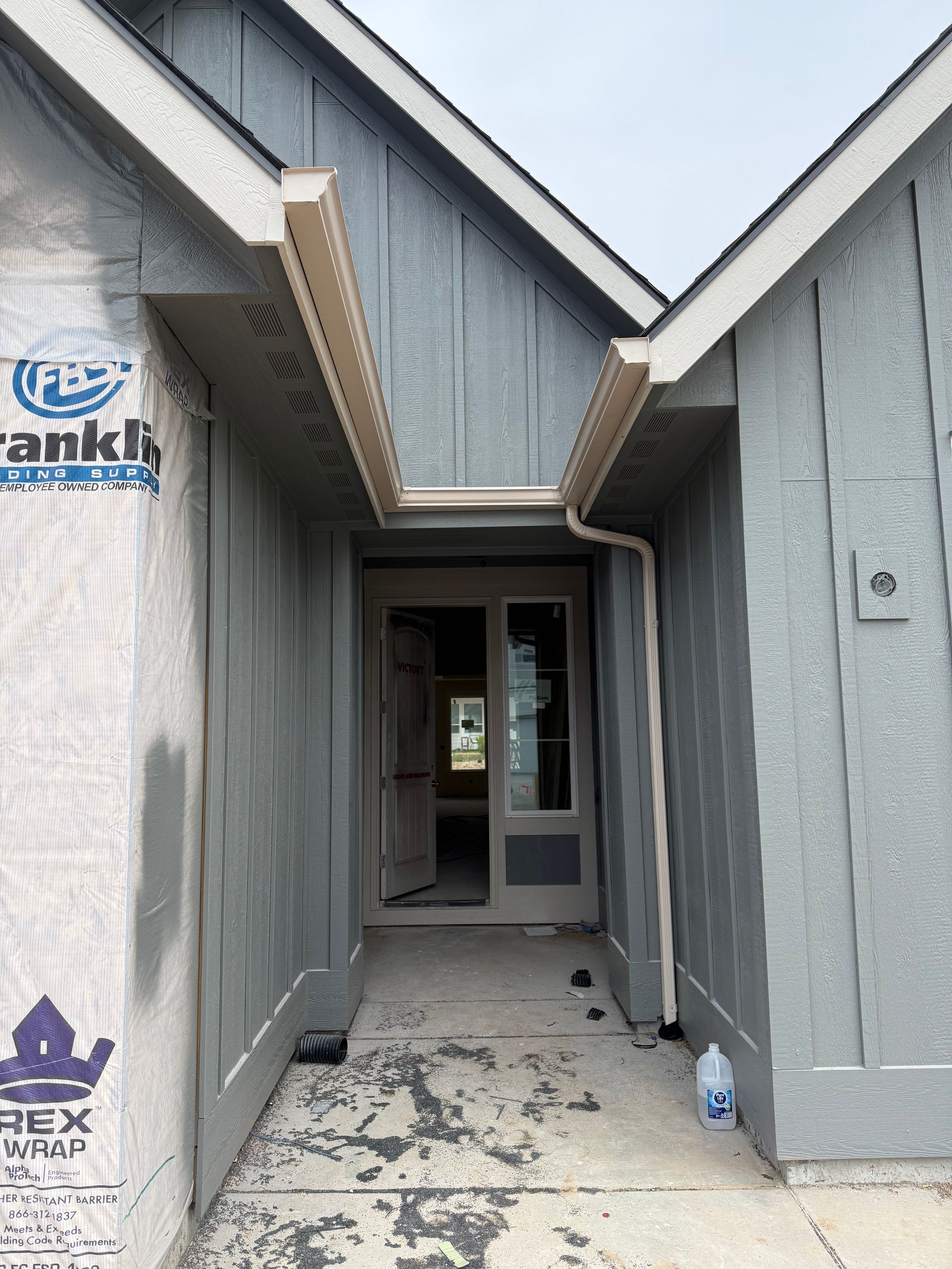 Covered entrance of a house under construction; gray siding, tan trim, open doorway.