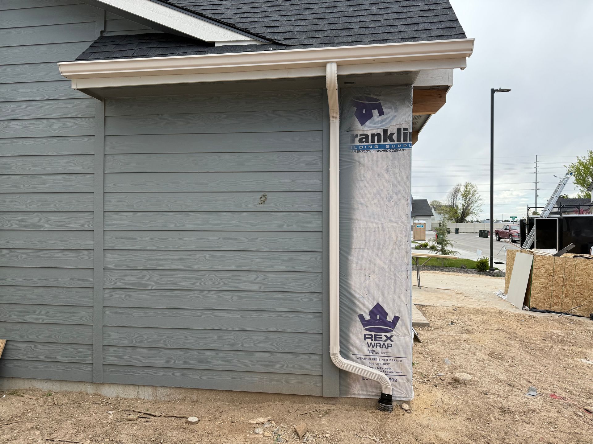 Exterior of a building under construction, featuring gray siding, a white gutter, and a drainpipe against a wrap.
