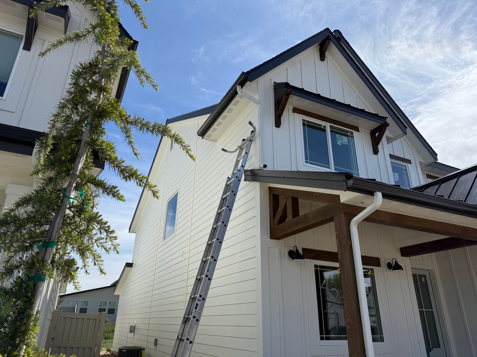 White house with black trim, a ladder, and a blue sky.