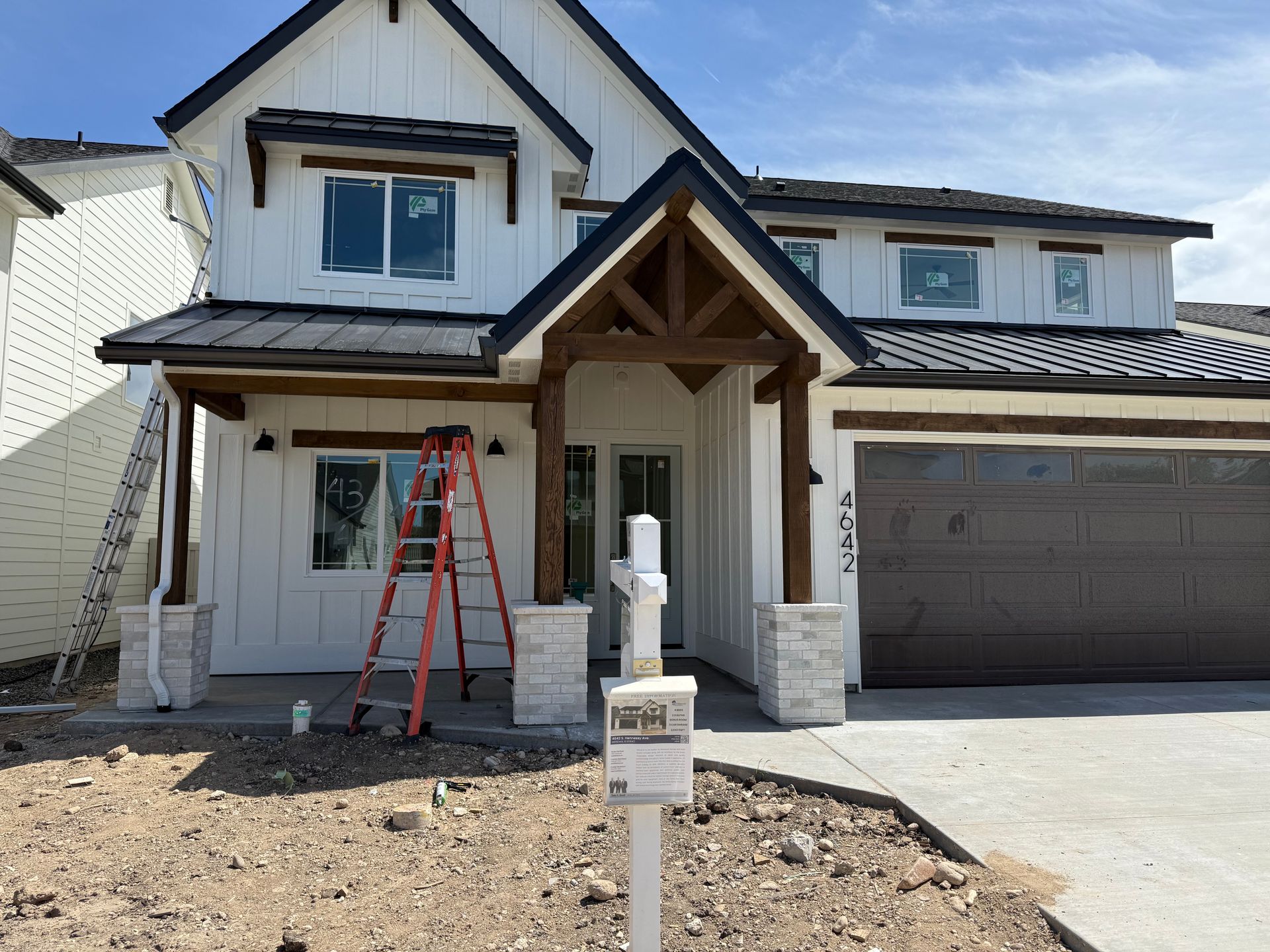 Two-story house with white siding, dark roof, wooden accents, and a brown garage door under construction.