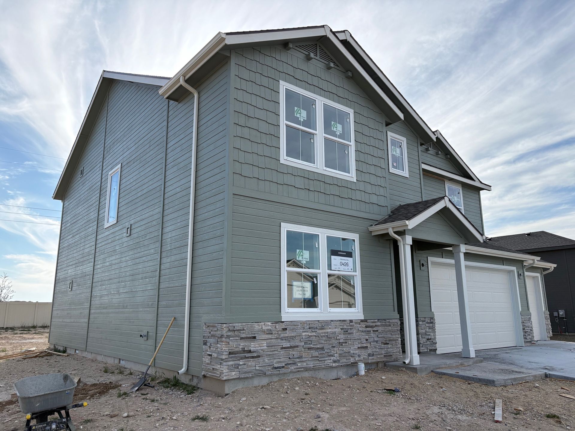 Two-story house under construction with gray siding, white trim, and a stone veneer on the lower front.