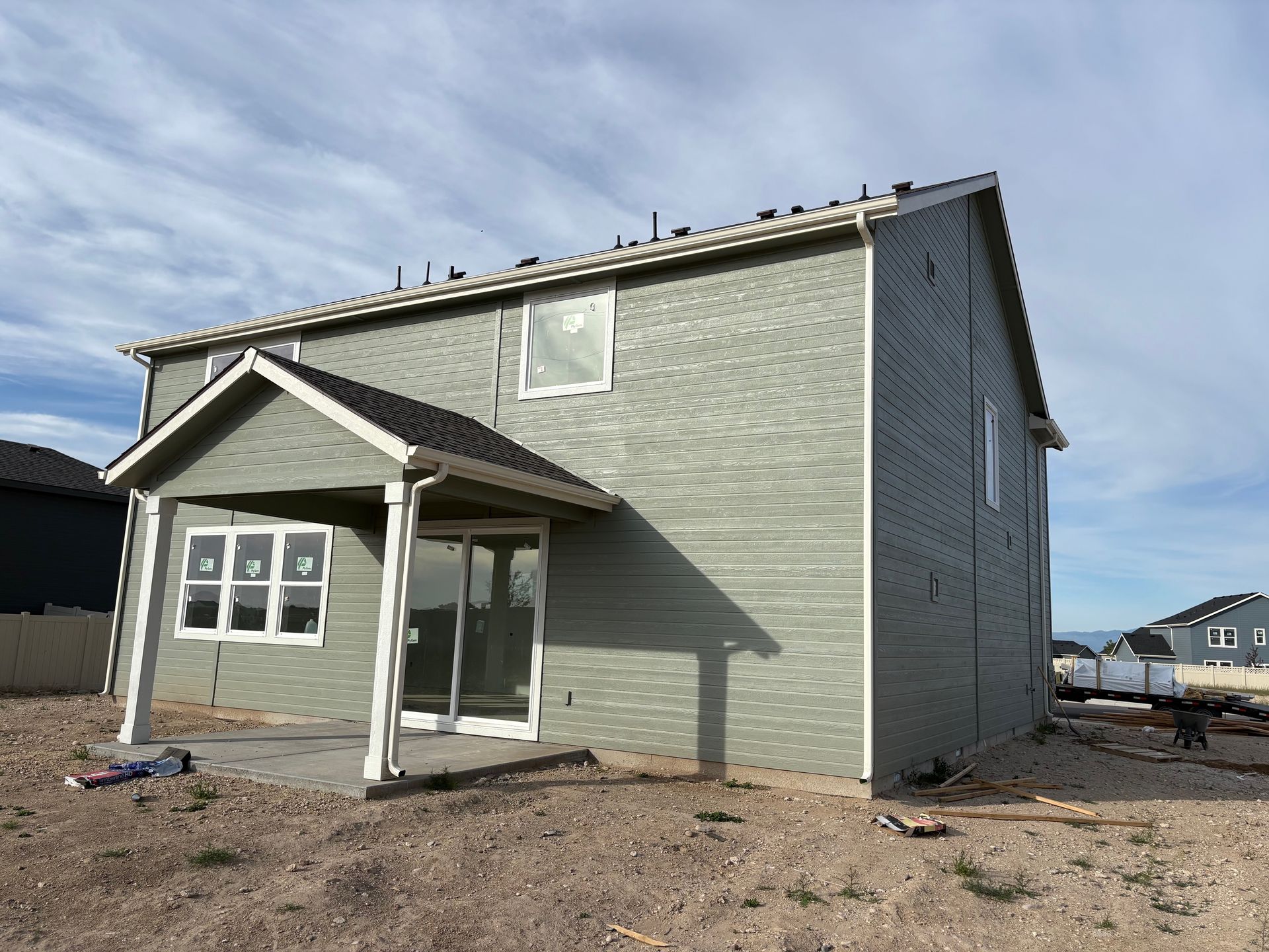 Two-story house with green siding, a covered porch with a patio, and a cloudy sky.