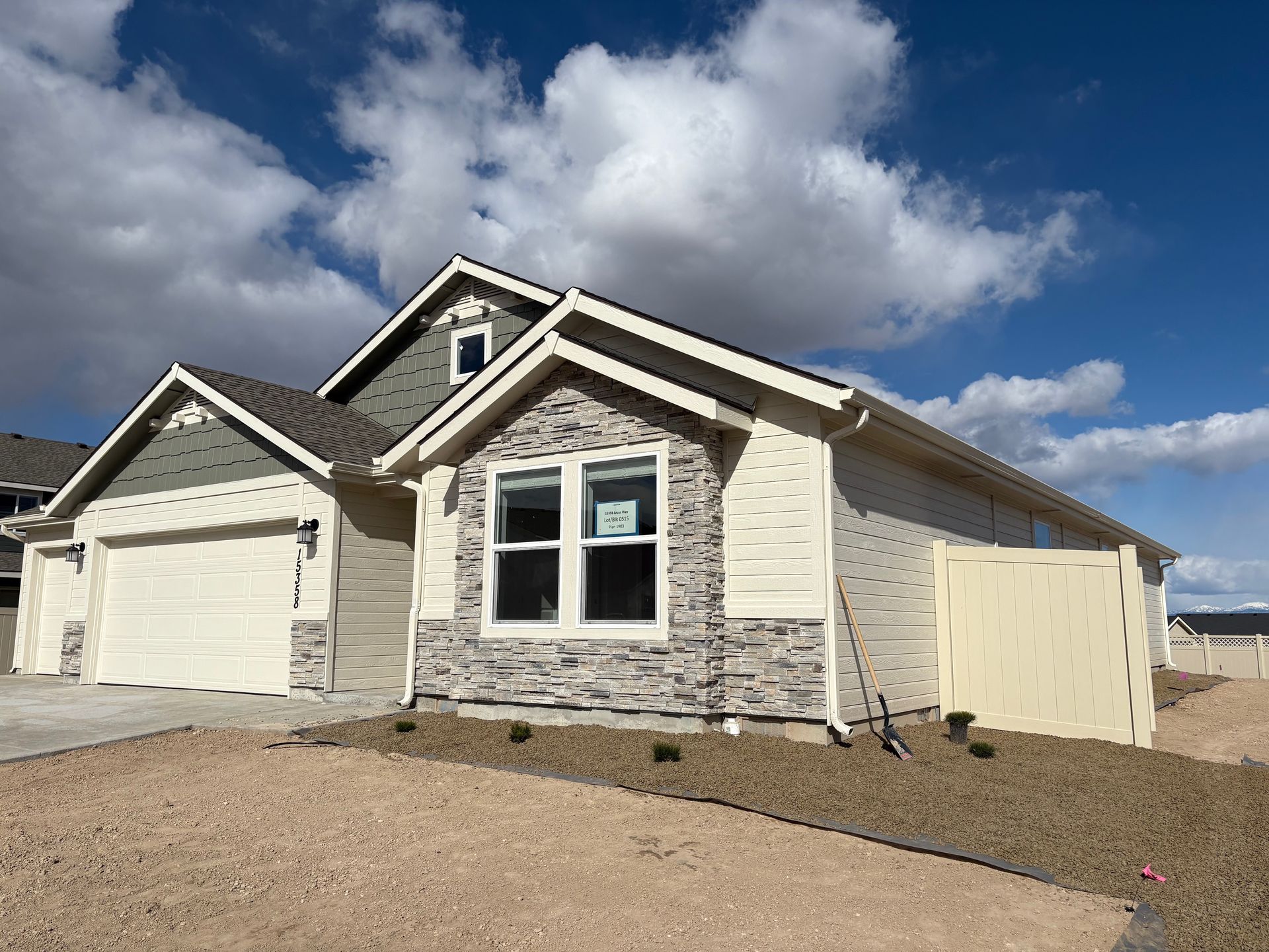 New beige house with grey stone and siding, cloudy sky.