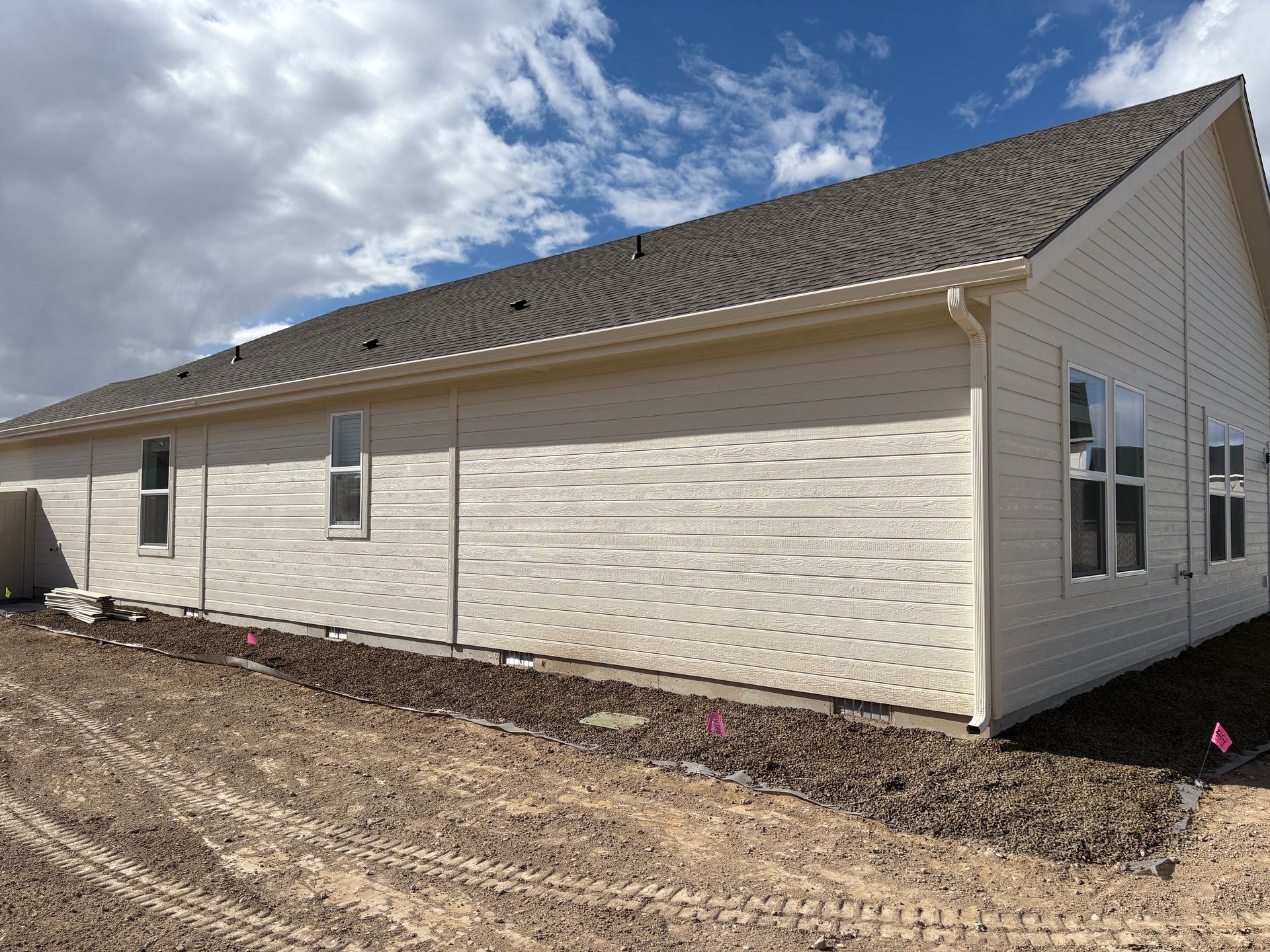 Tan siding on a long, single-story building with a brown roof under a partly cloudy sky.