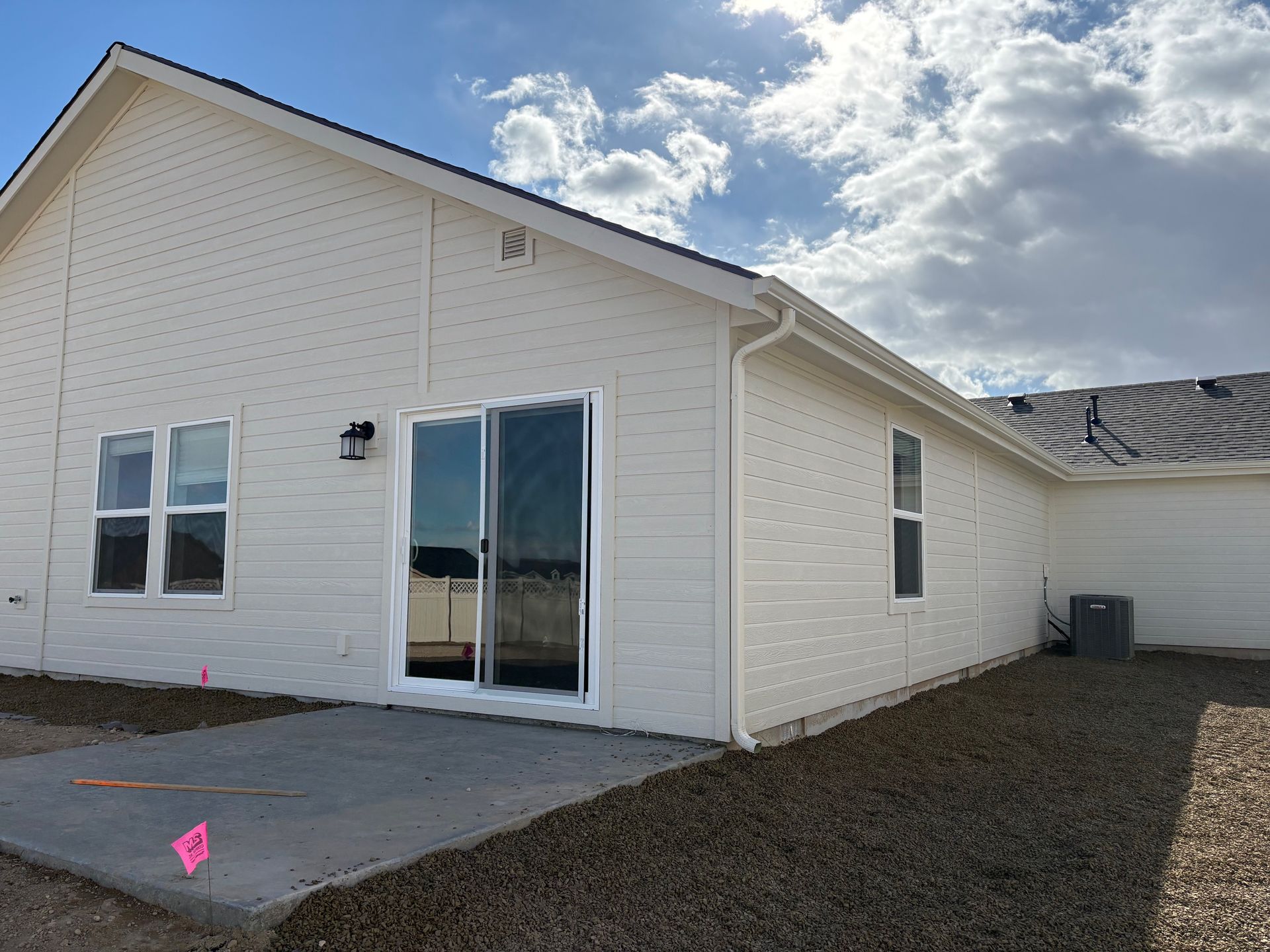 Back exterior of a cream-colored house with a concrete patio, sliding glass door, and two windows.