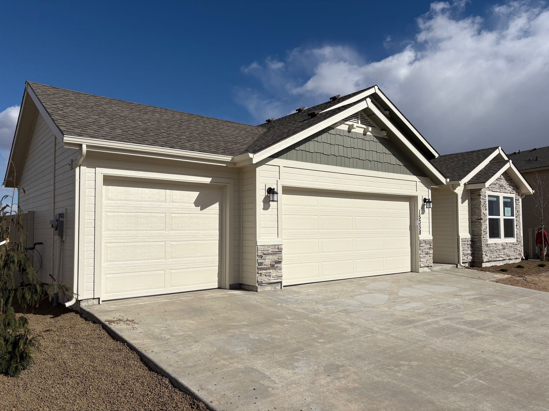 Tan house with a two-car garage, grey roof, and stone accents.