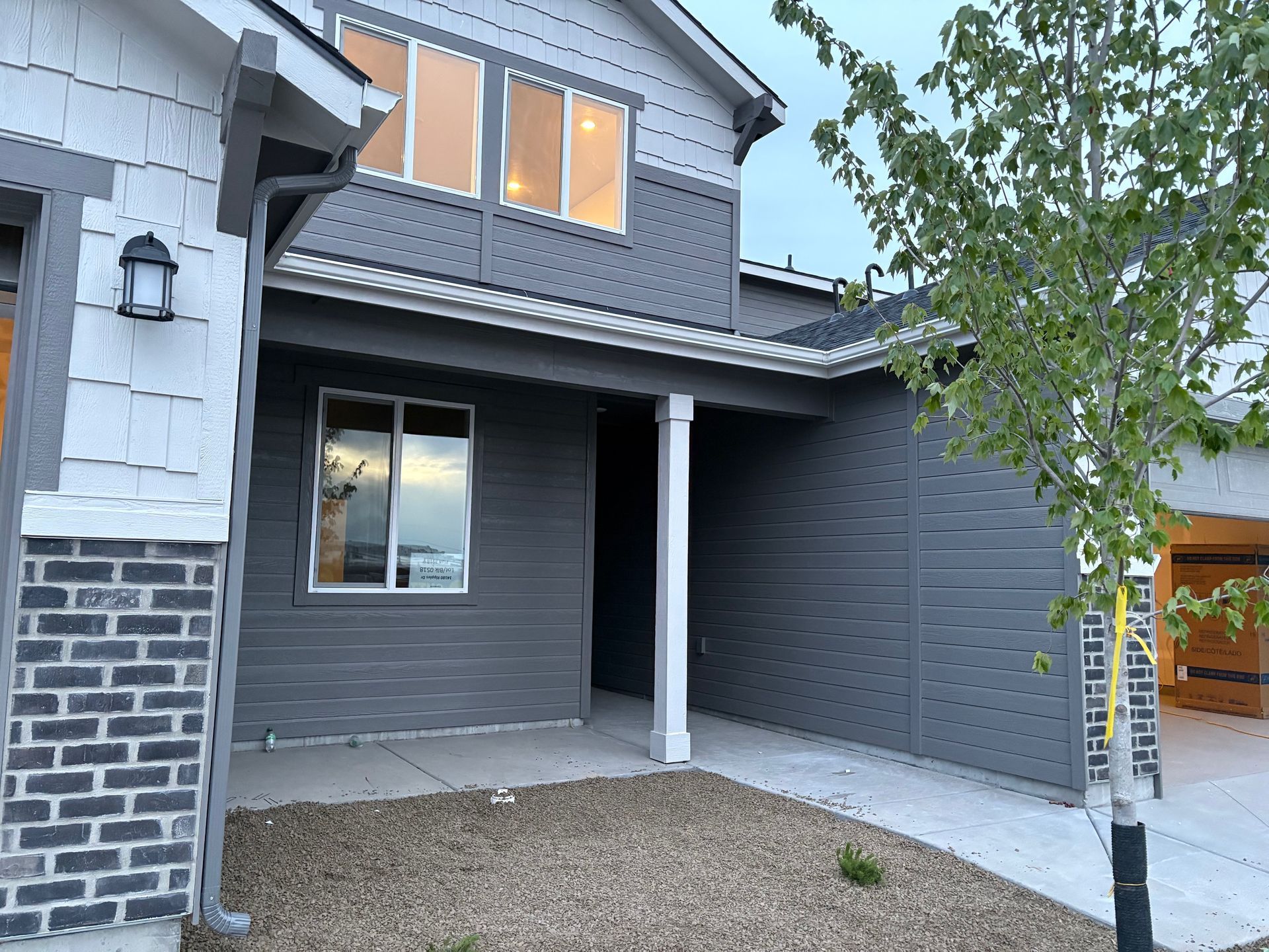 A two-story house with gray siding, white trim, and a small front yard with gravel.