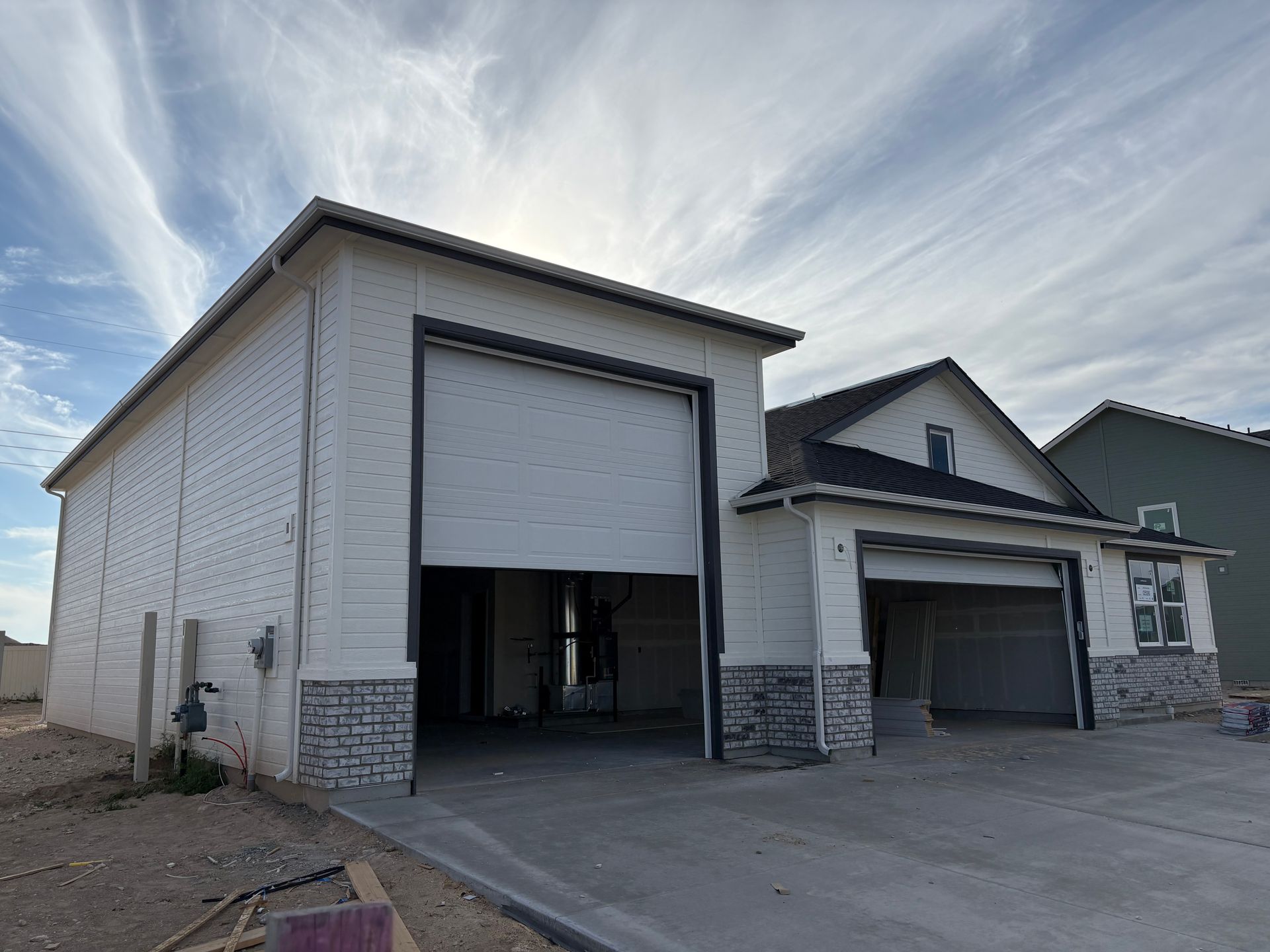Two-story house with open garage doors. White brick exterior, gray stone accents, concrete driveway, and cloudy sky.