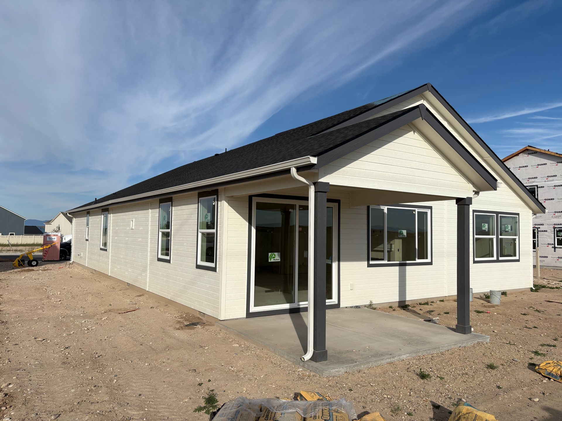 New construction house with beige siding, dark trim, and a small patio under a blue sky.