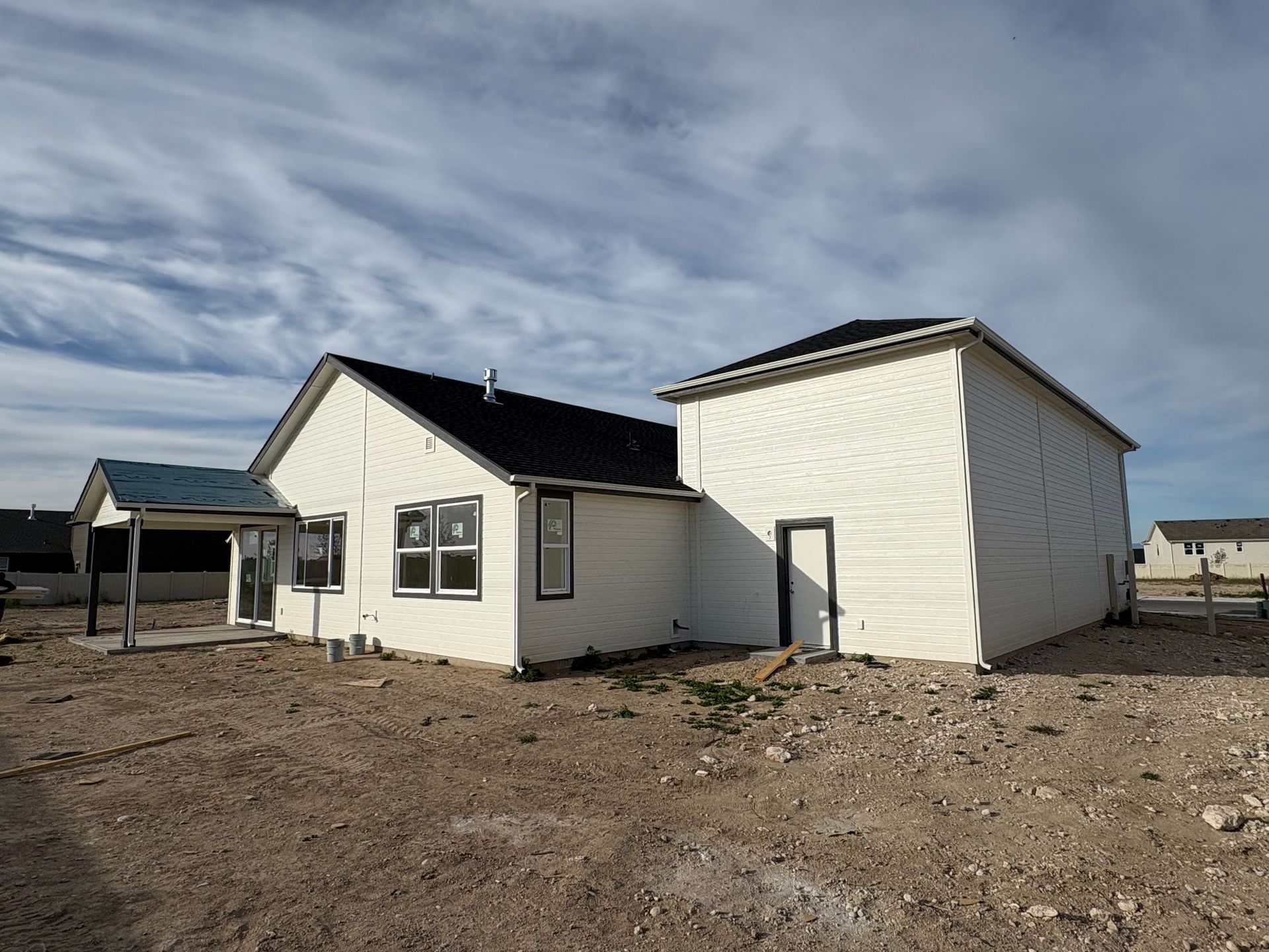 White house with black roof, side view. Backyard is dirt. Cloudy sky overhead.