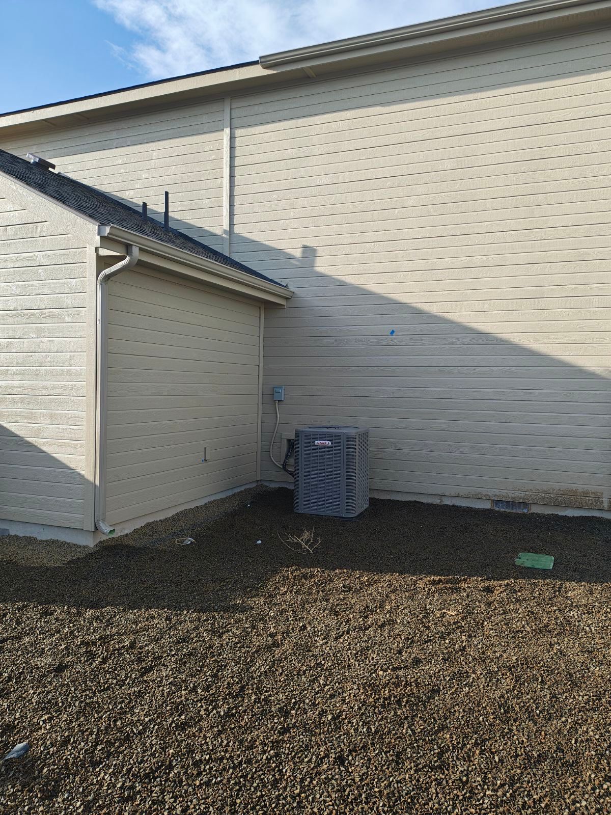 Exterior of a building with light tan siding. An air conditioning unit sits on the ground.