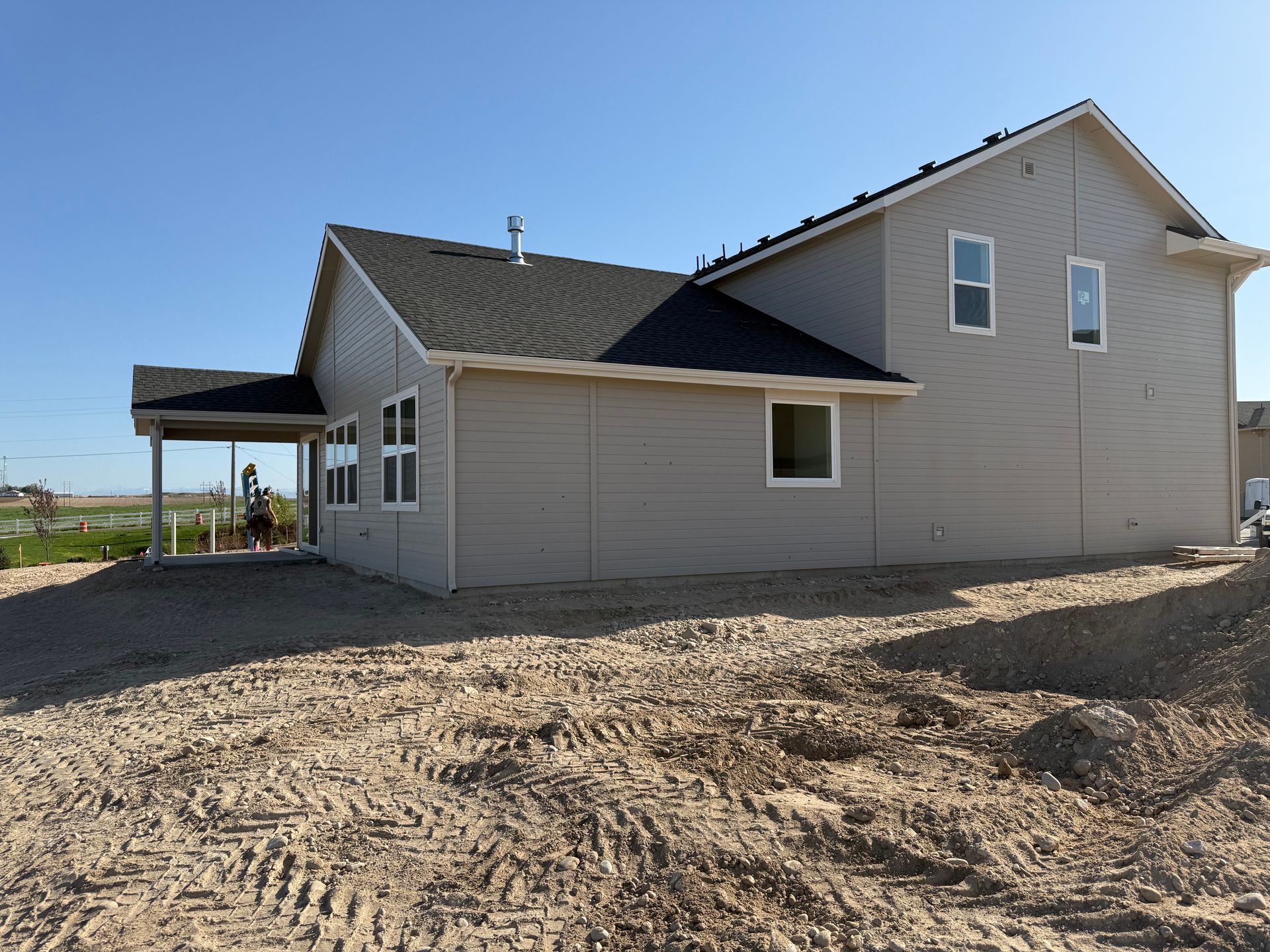 Beige house under construction, with a covered patio and gravel yard.