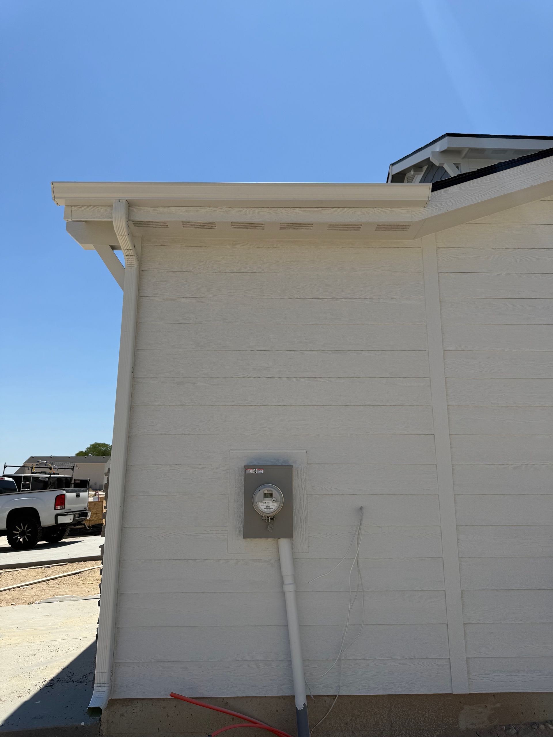 White siding on building with gutter, electrical meter, and conduit on a sunny day.