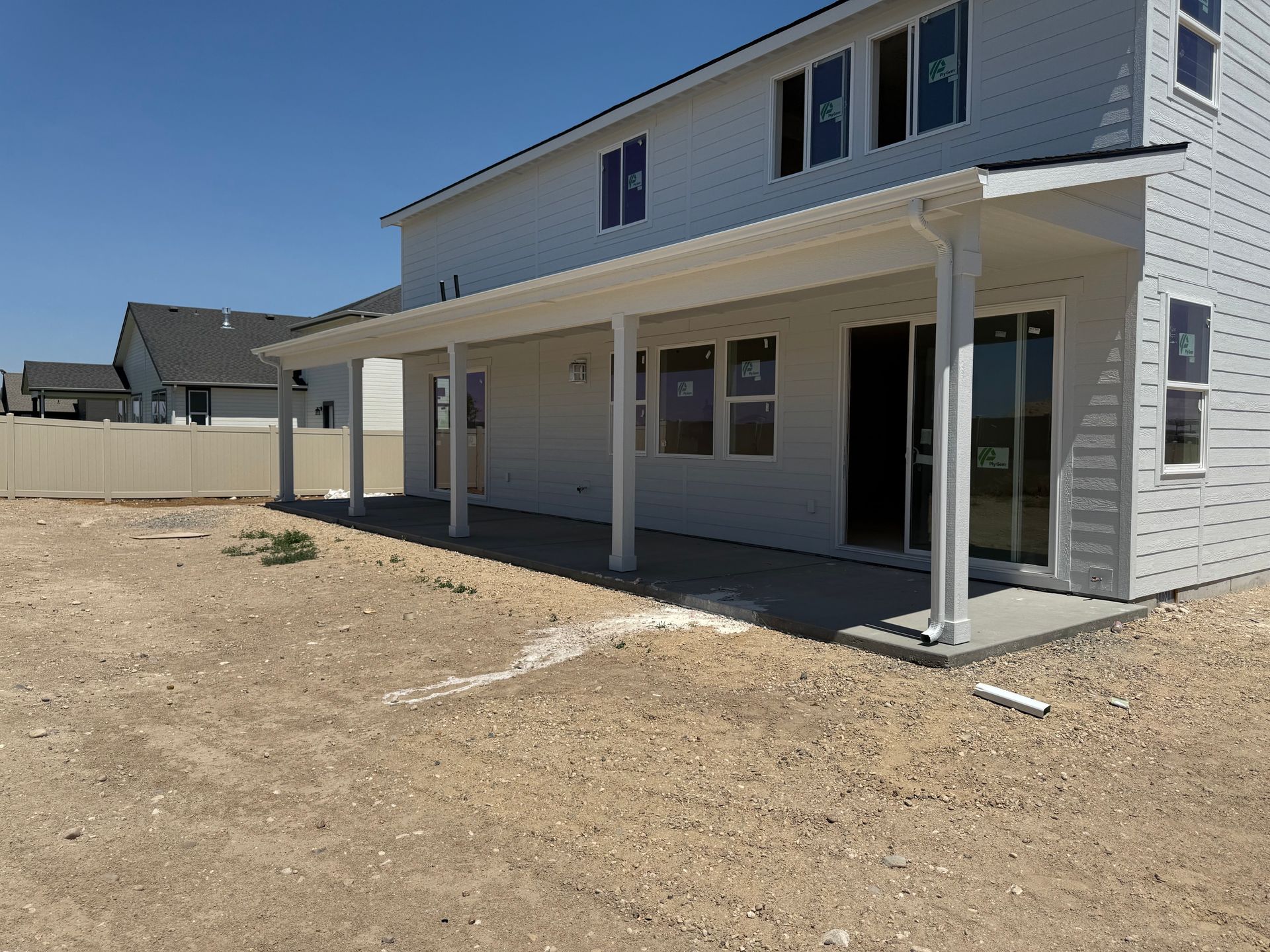 Backyard view of a two-story white house with a covered patio, on a gravel lot.