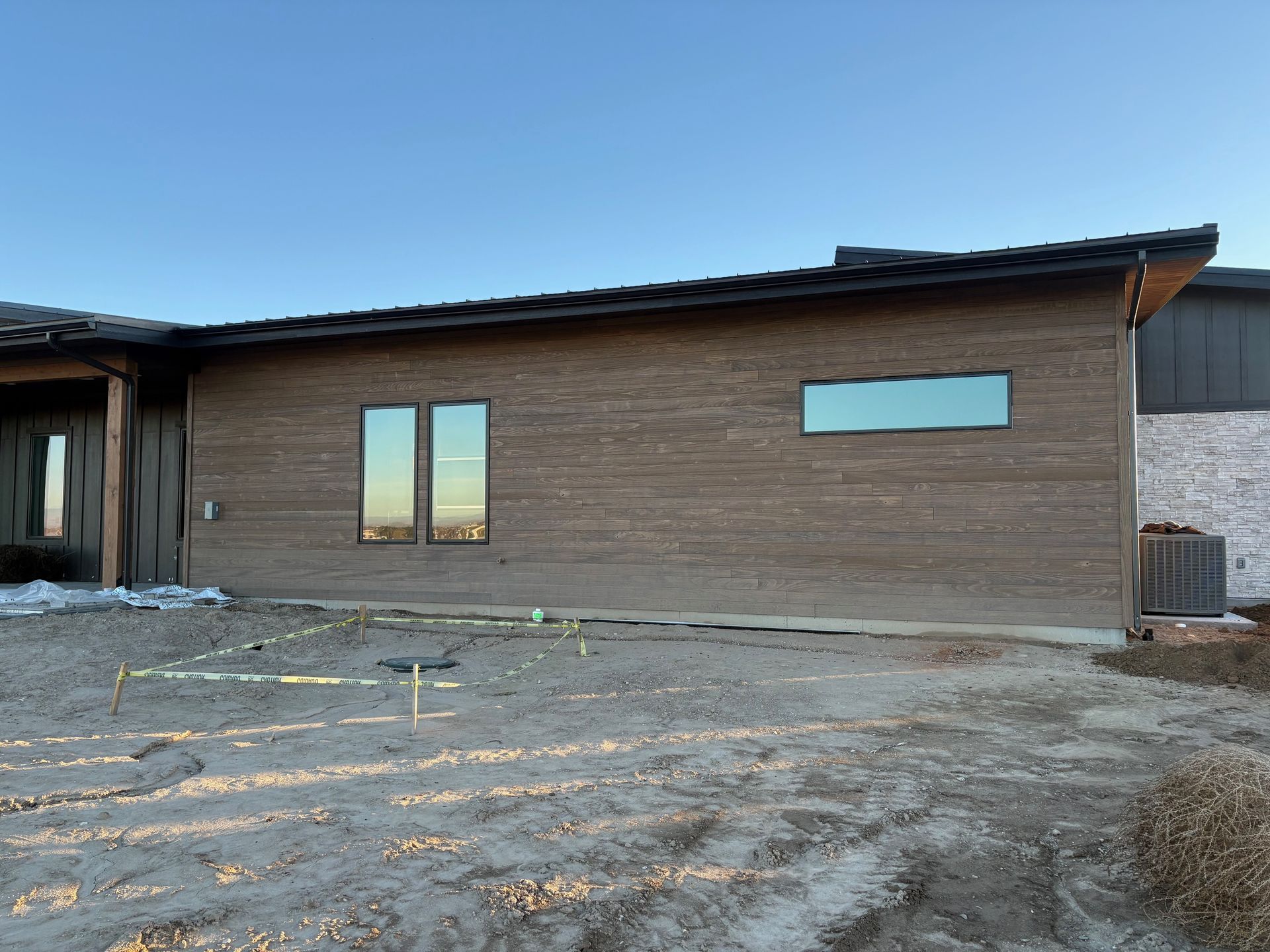 Exterior of a modern house under construction; brown siding, rectangular windows, sloping roof, dirt yard.