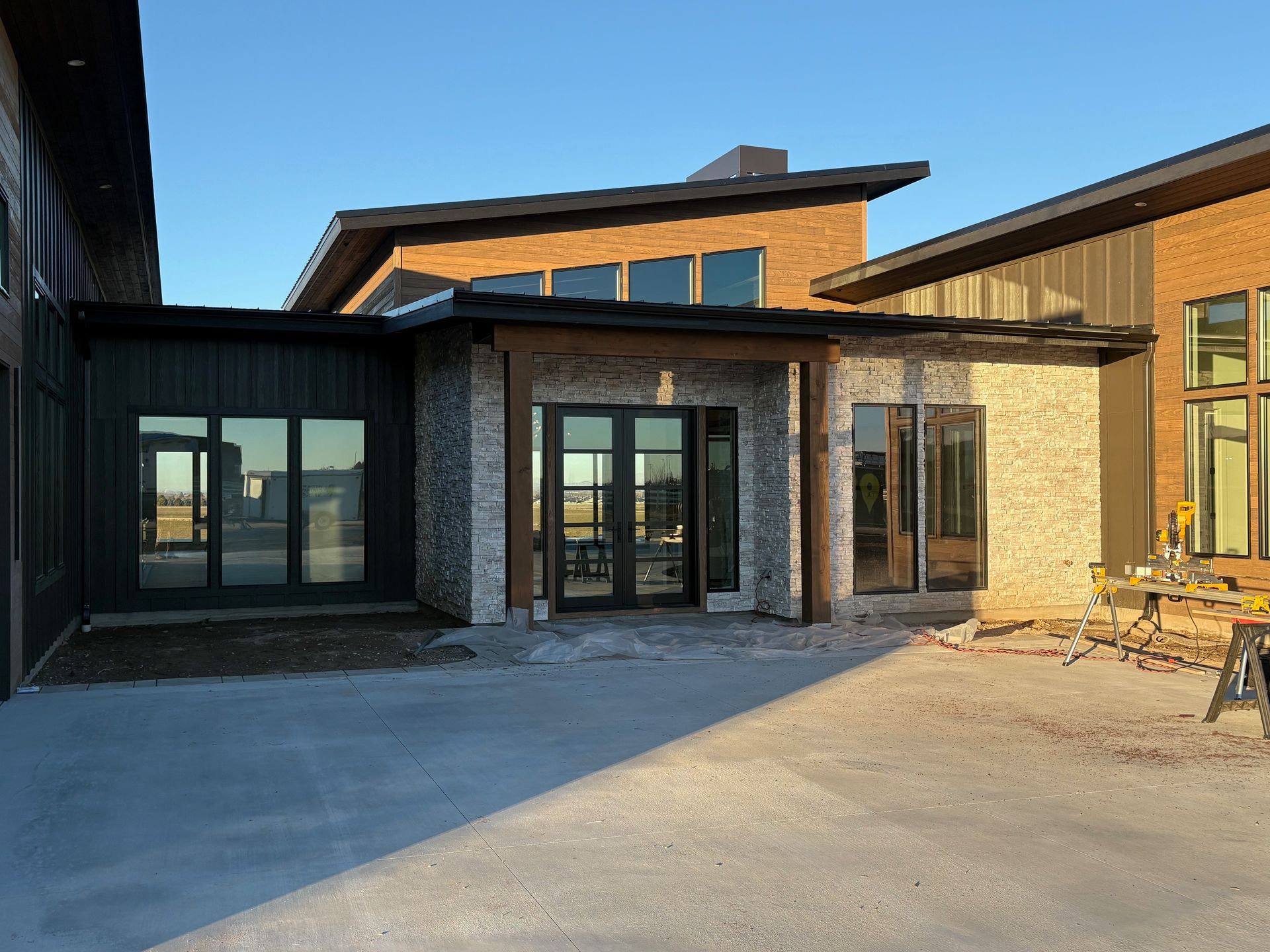 Exterior of modern home with brick, wood, and dark metal accents. Glass doors and windows. Sunny, outdoor setting.