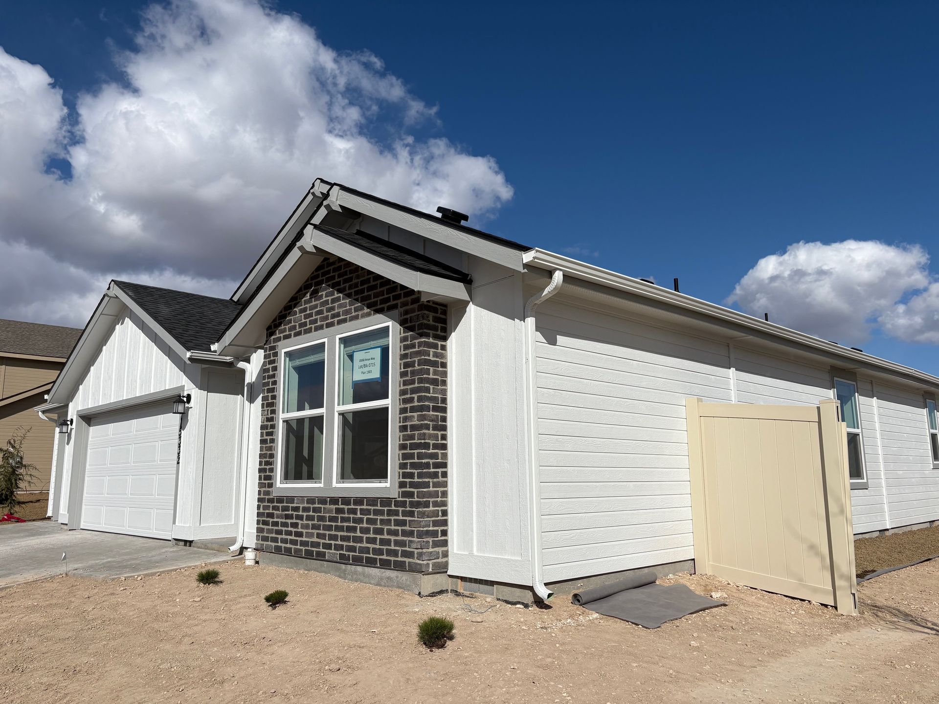 Newly constructed house, white siding, black roof, brick accent, against a blue sky, gravel yard.