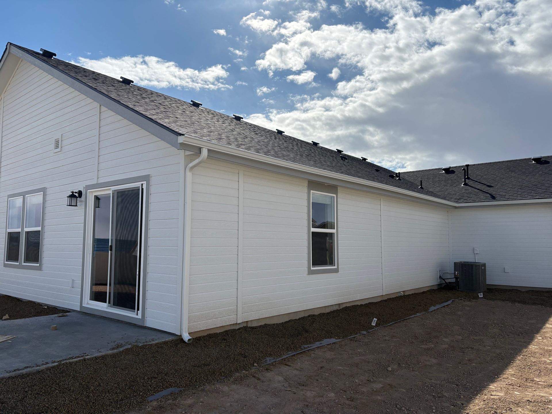 White house exterior with dark roof, windows, and sliding glass door. Overcast sky.