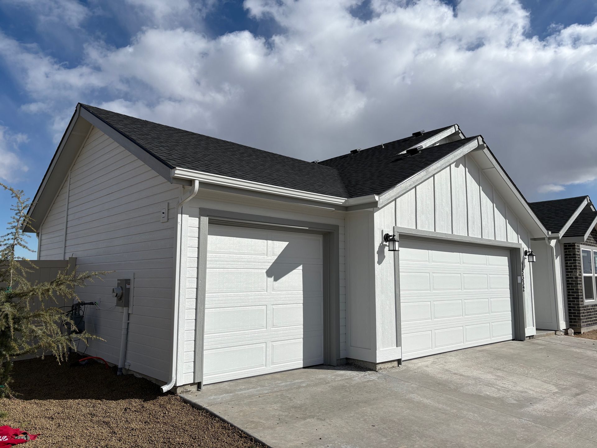 White house with black roof, two-car garage. Overcast sky.