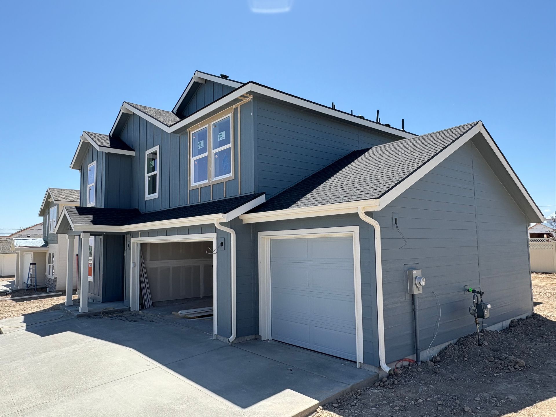 Two-story blue house with white trim and two attached garages on a sunny day.