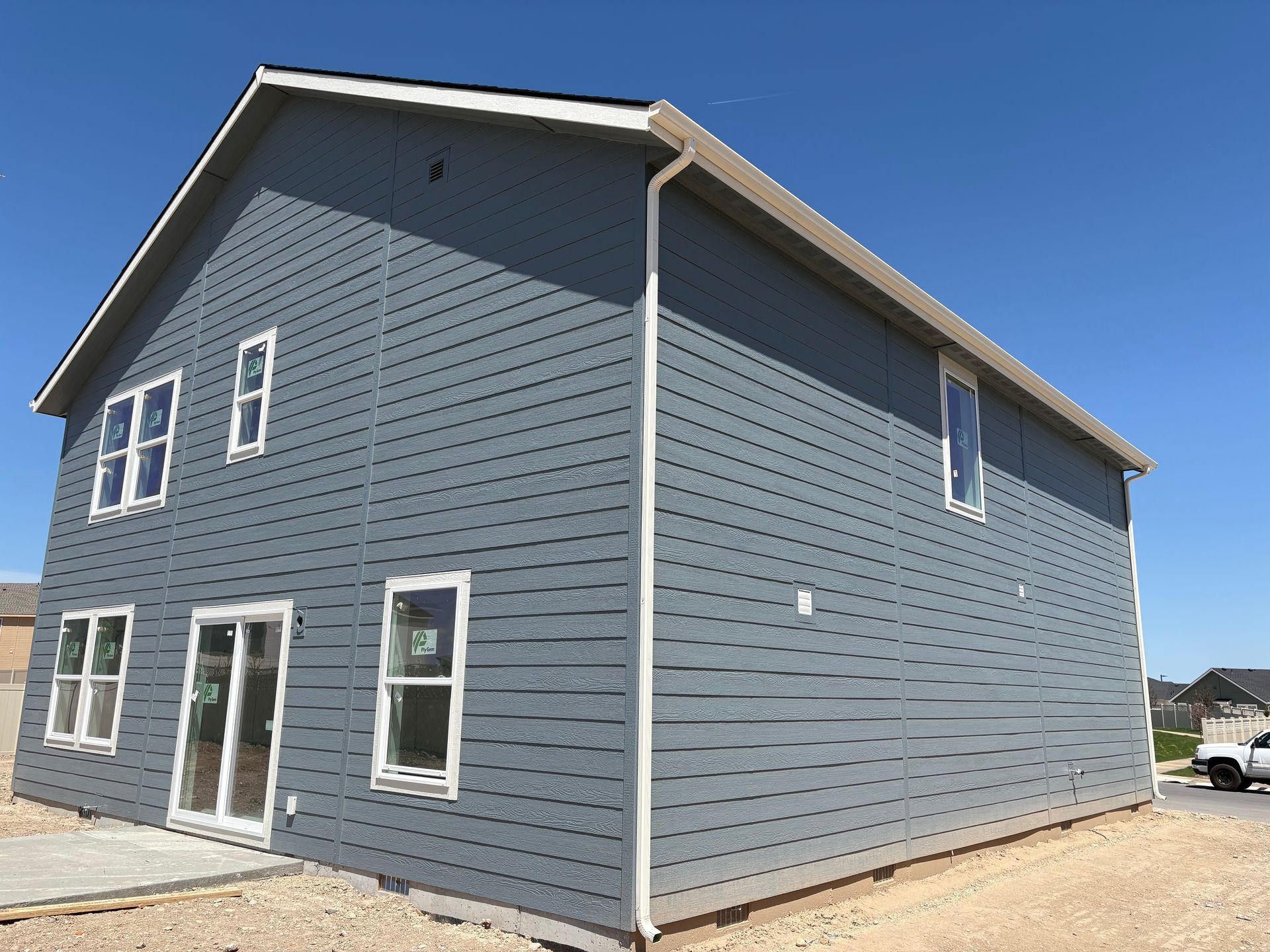 Two-story house under construction, blue-gray siding, white trim, sliding glass doors, clear blue sky.