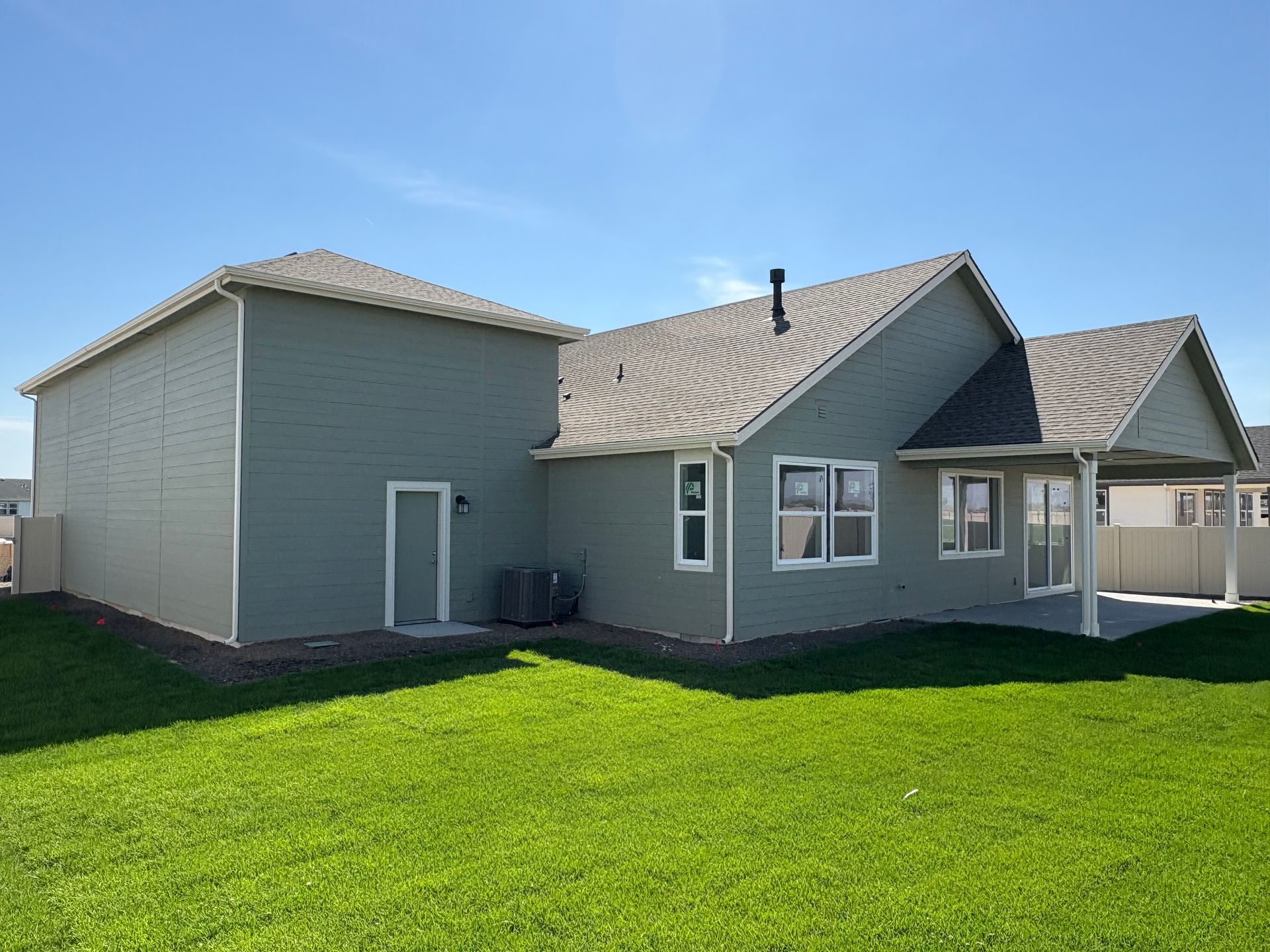 Green house exterior with a grassy yard under a bright blue sky.