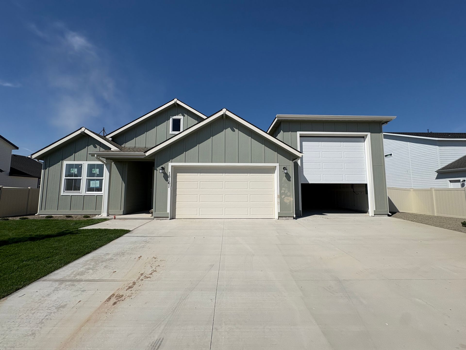 Light green house with white garage door and concrete driveway under a clear, blue sky.