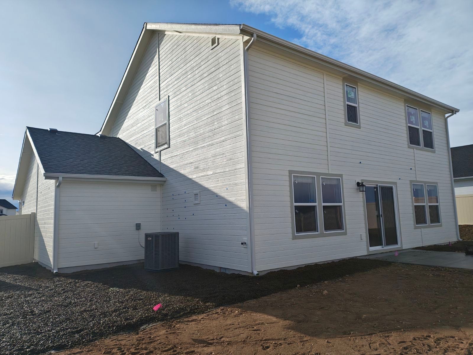 Back of a two-story white house with a small attached roof. Blue sky, brown earth.