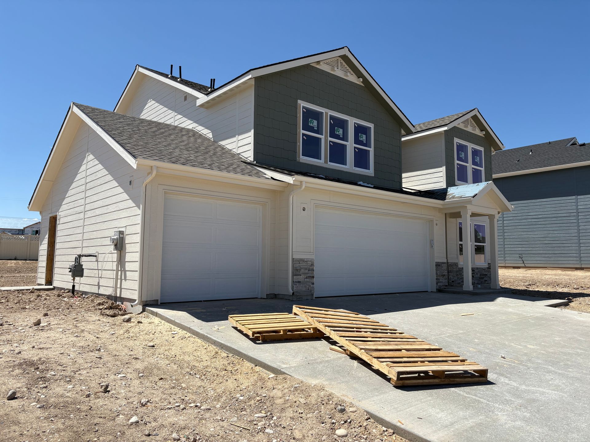 Two-story house under construction with white siding, grey accents, and two-car garage.