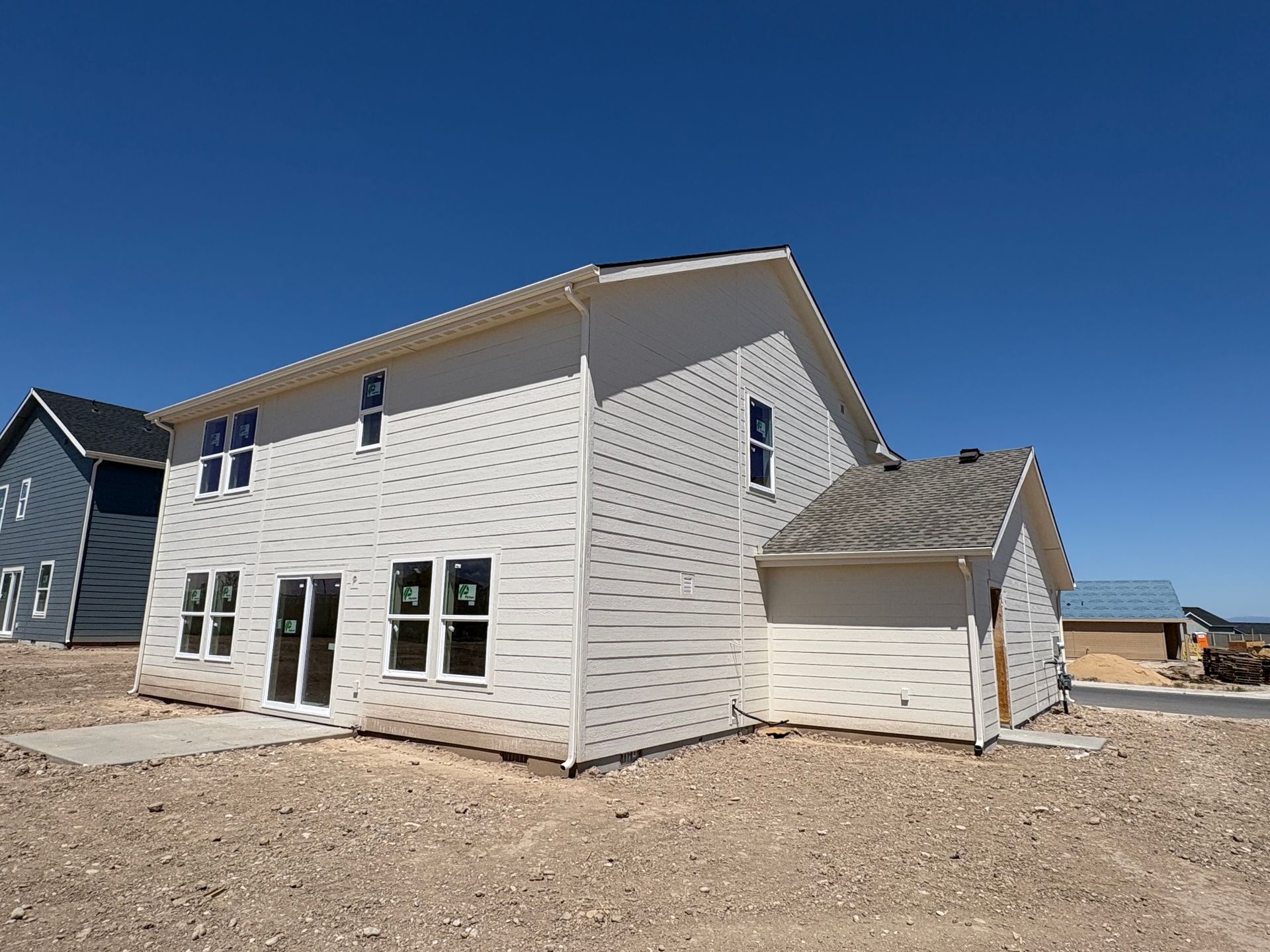 Two-story house under construction with white siding on a gravel lot under a blue sky.