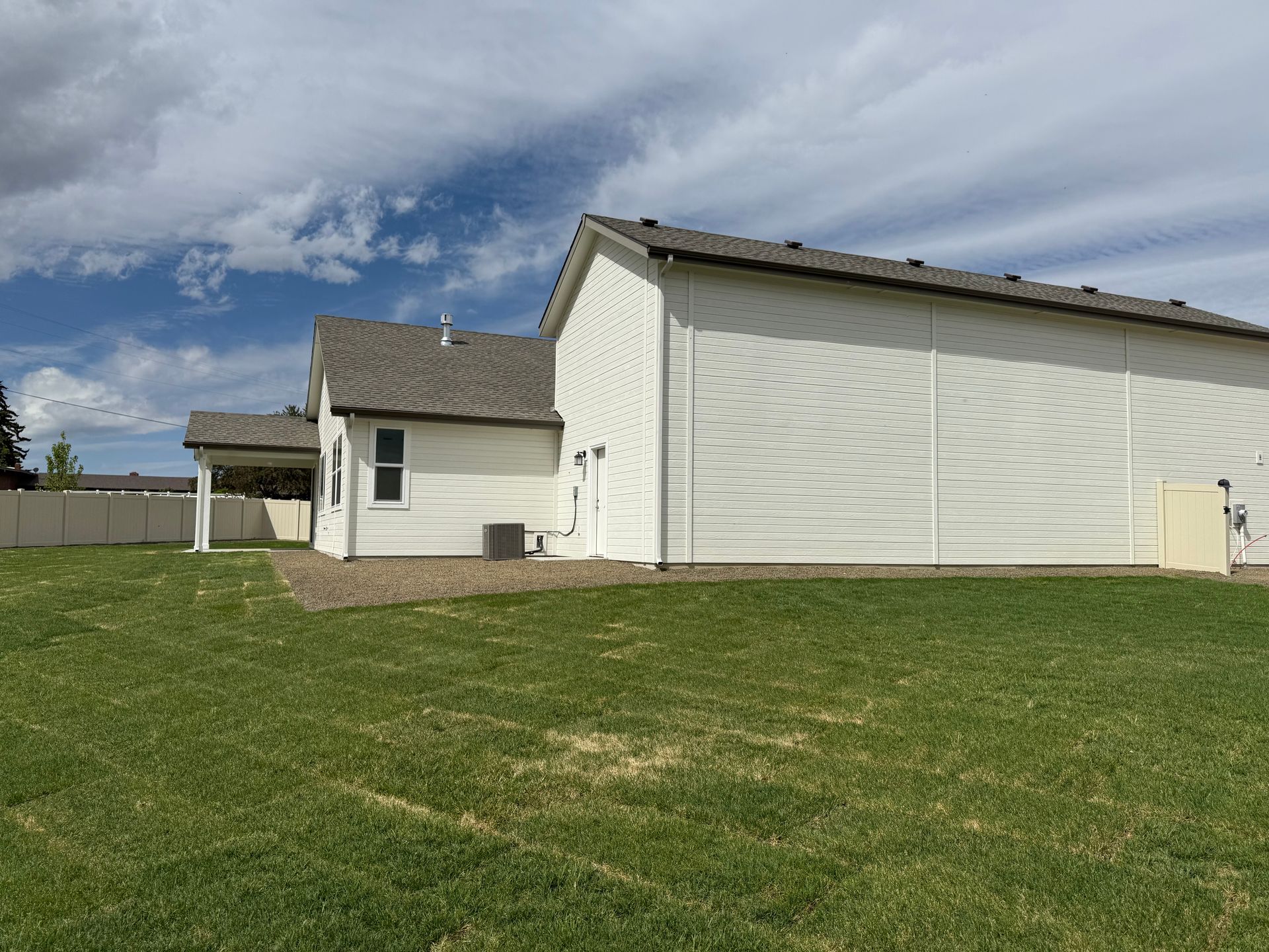 White house with gray roof, green lawn, cloudy sky.