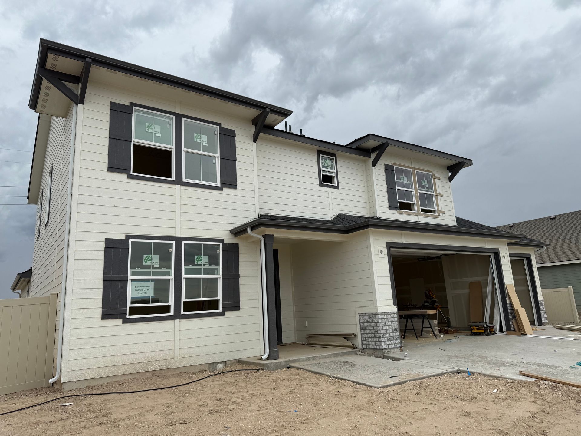 Two-story house under construction with white siding, dark shutters, and a garage; cloudy sky.