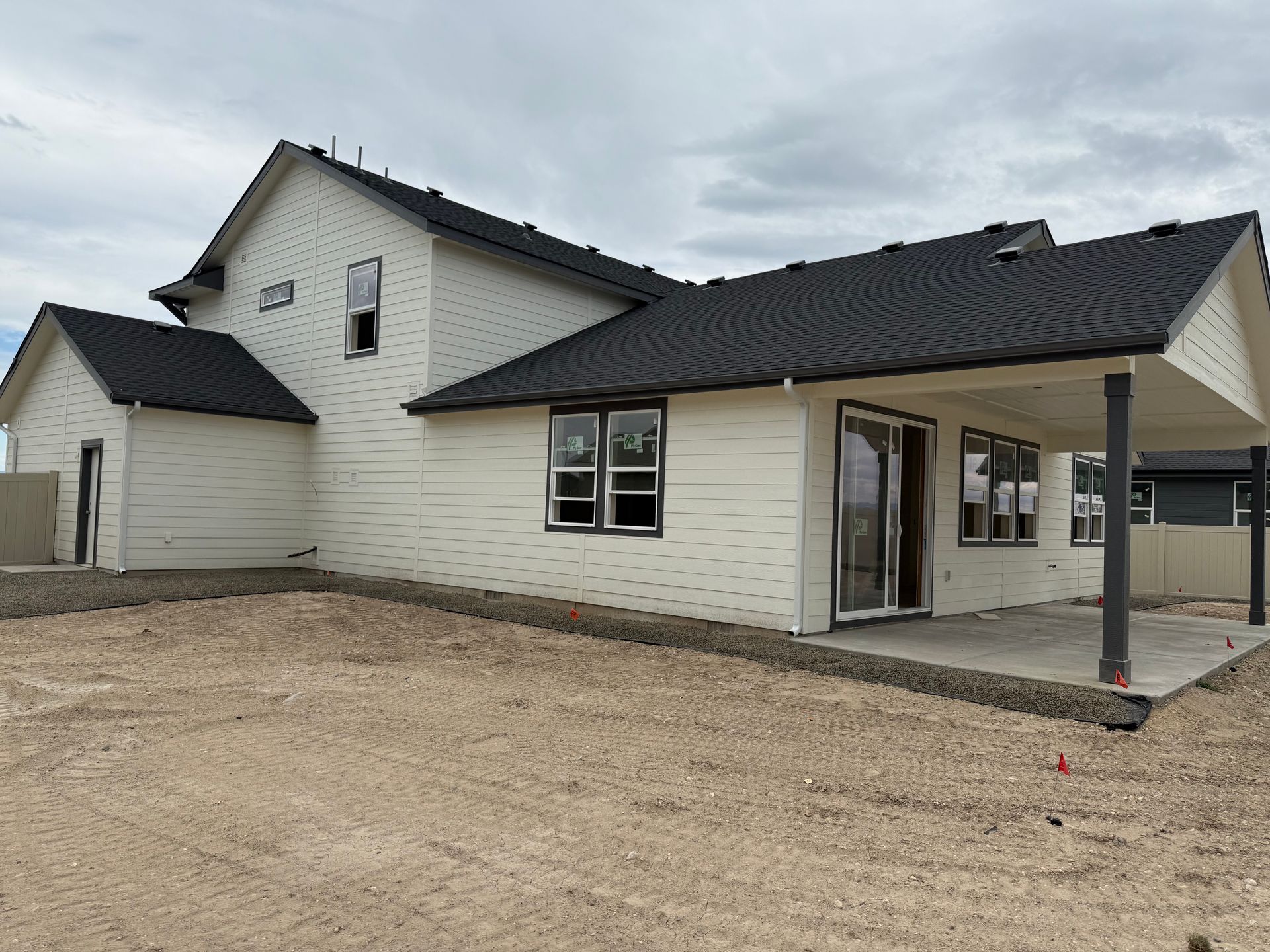 Exterior view of a two-story house with light siding and a dark roof, in a construction setting.