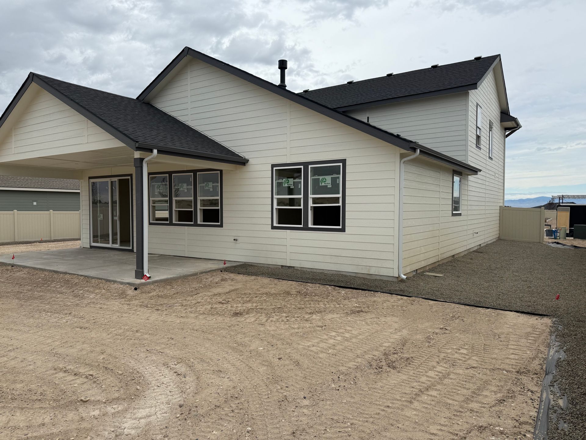 Back of a new two-story house with light siding and black roof. Unfinished yard with gravel and dirt.