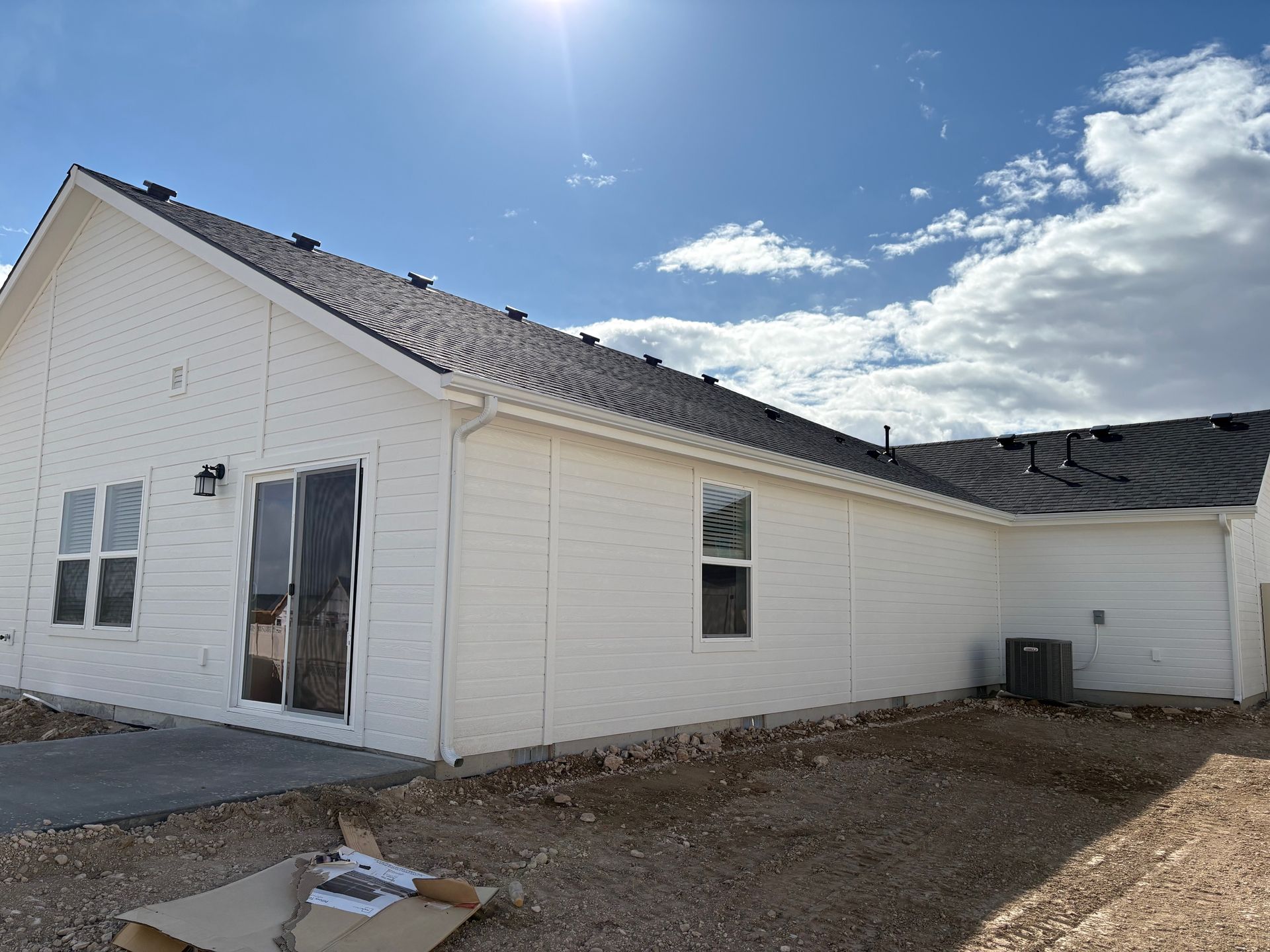 Back of a white house with a dark roof and a small patio on a sunny day.