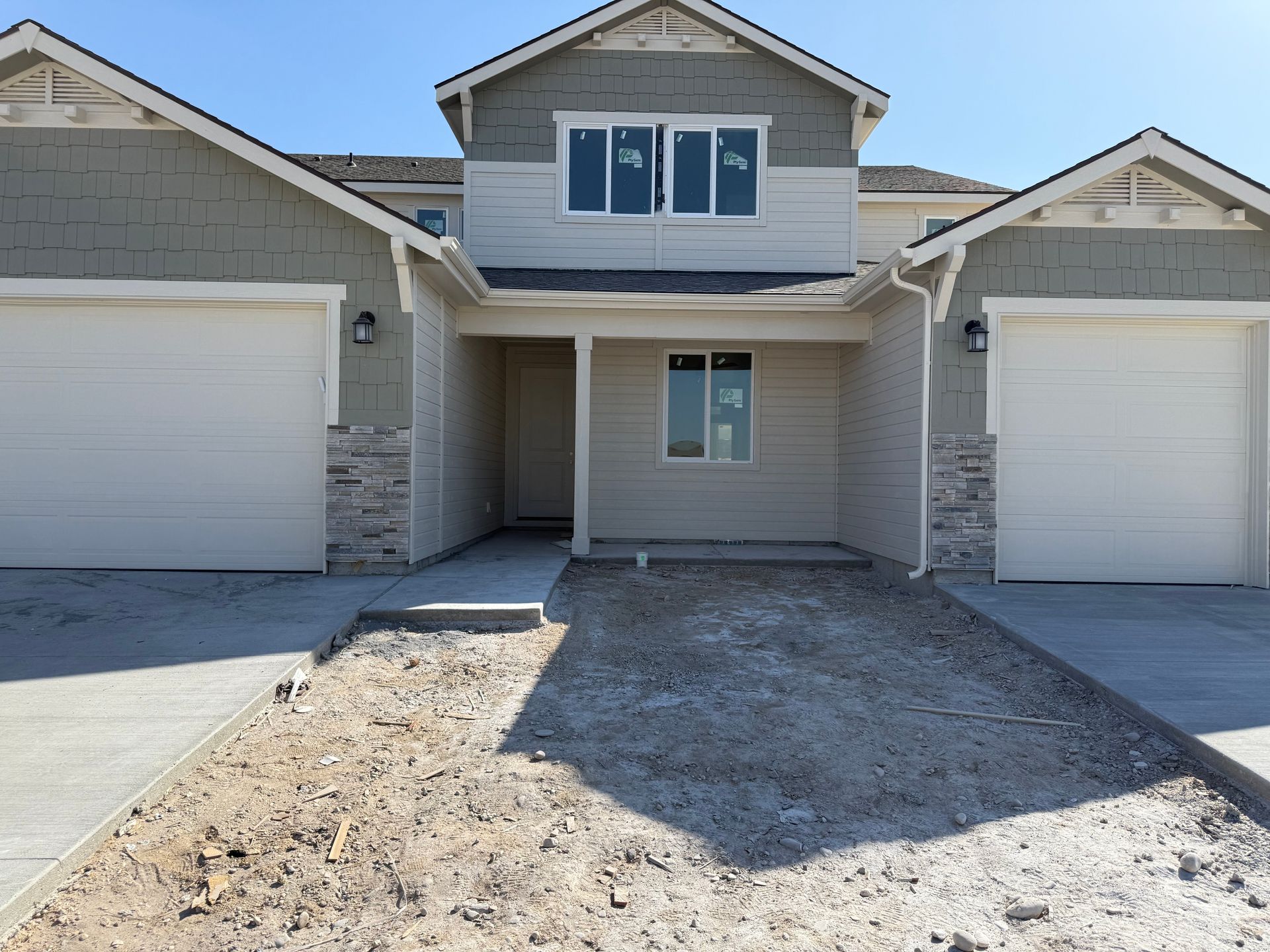 Newly constructed multi-unit home with two garages and a central entrance. Grey siding, stone accents, and concrete drive.
