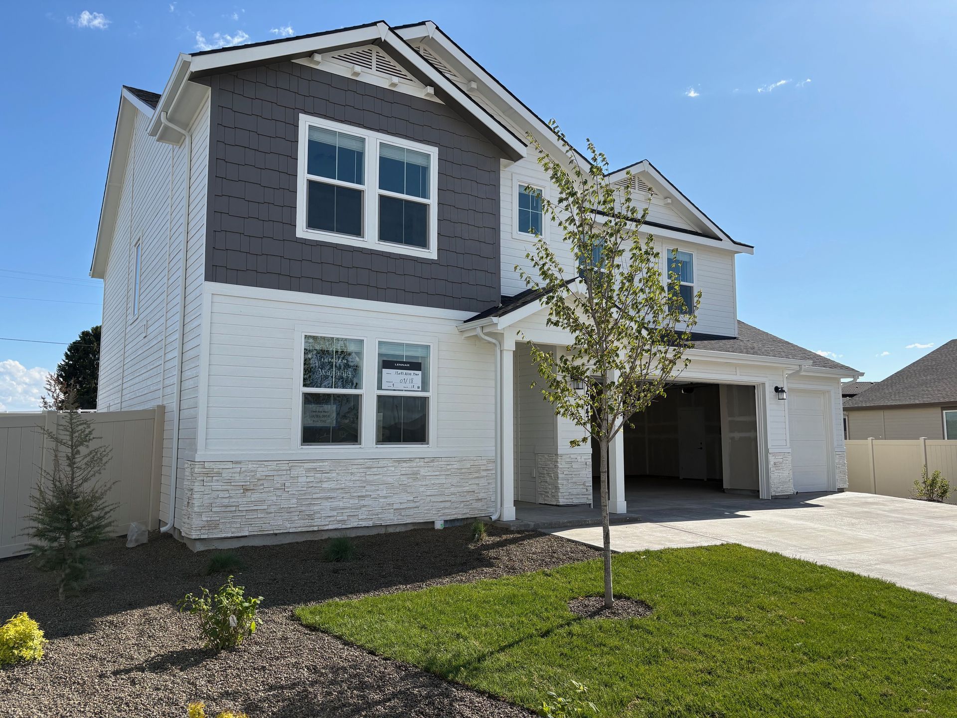 Two-story house with gray and white siding, open garage, and small tree in front yard.